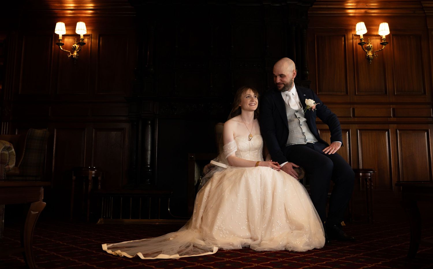 Wedding couple seated in an elegant room with warm lighting and vintage decor.