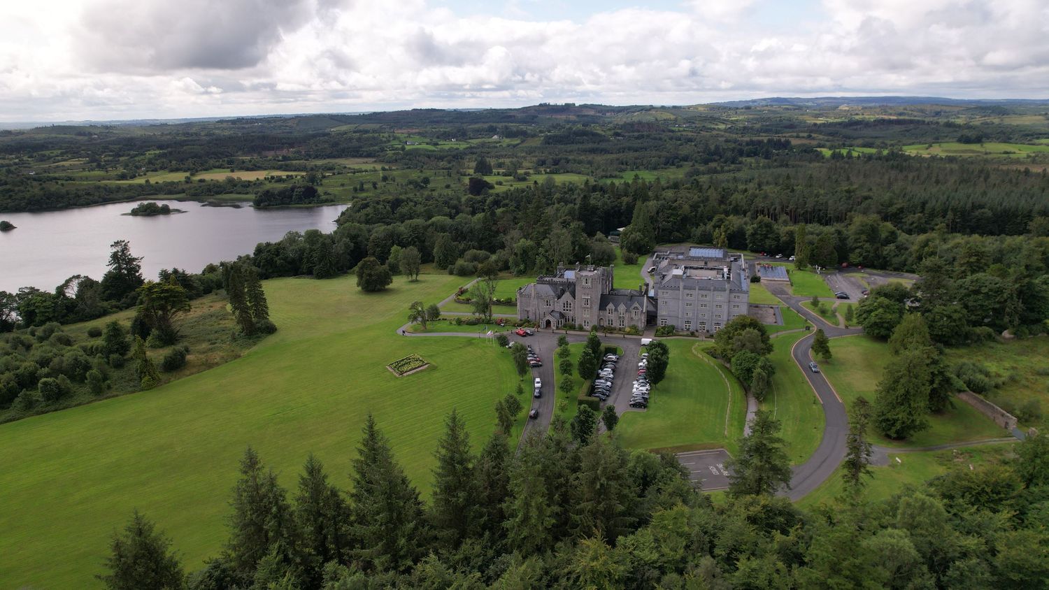 Panoramic view of lakeside estate with extensive grounds and tree-lined driveway.
