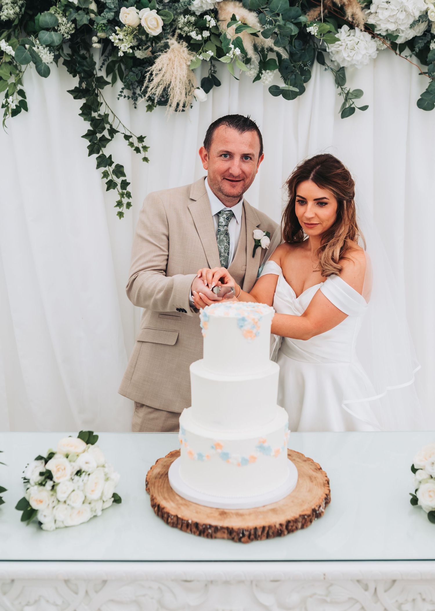A happy bride and groom cut their three-tier white wedding cake decorated with pastel confetti dots.