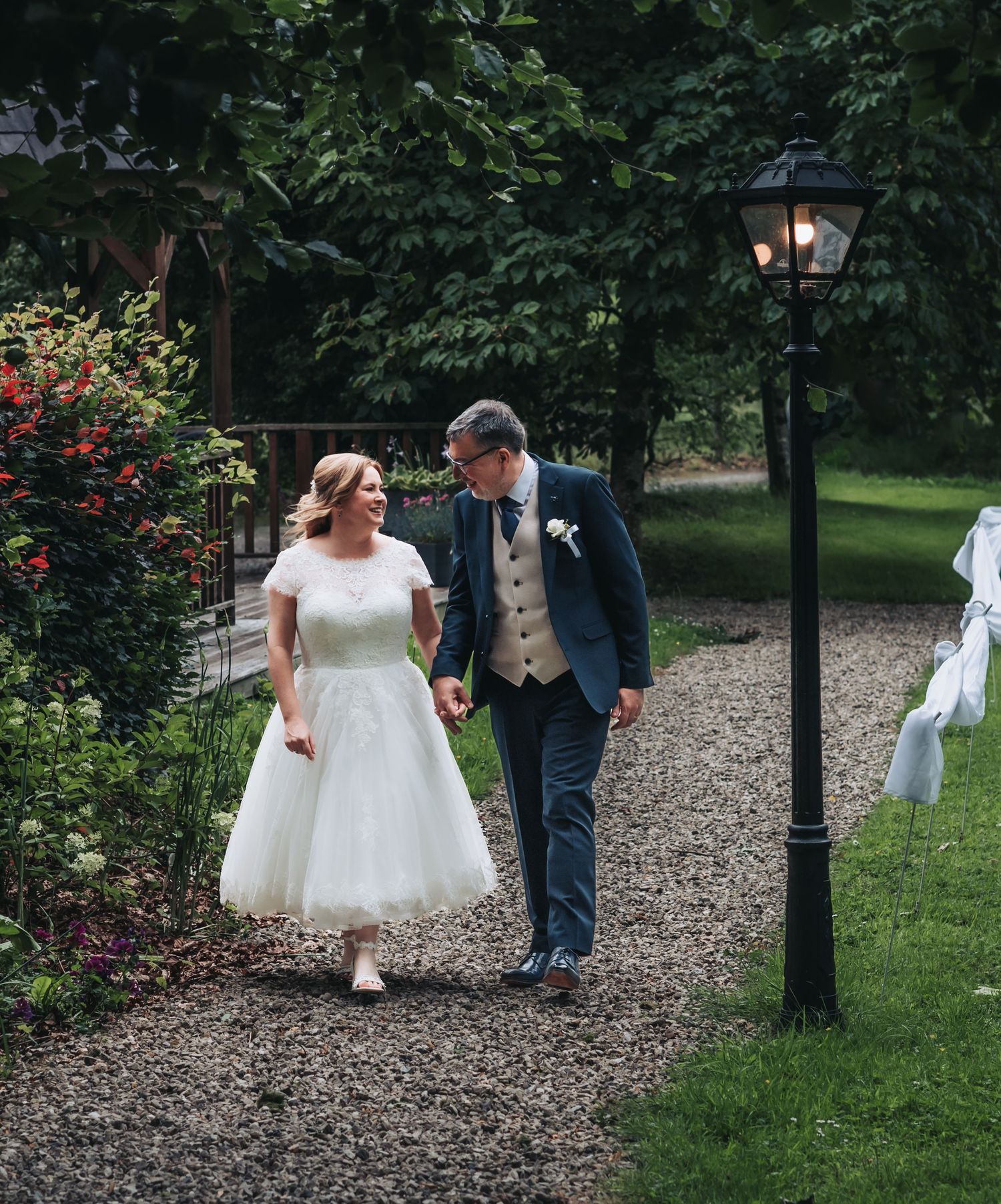 A couple walks along a garden path surrounded by greenery and flowers on their wedding day.