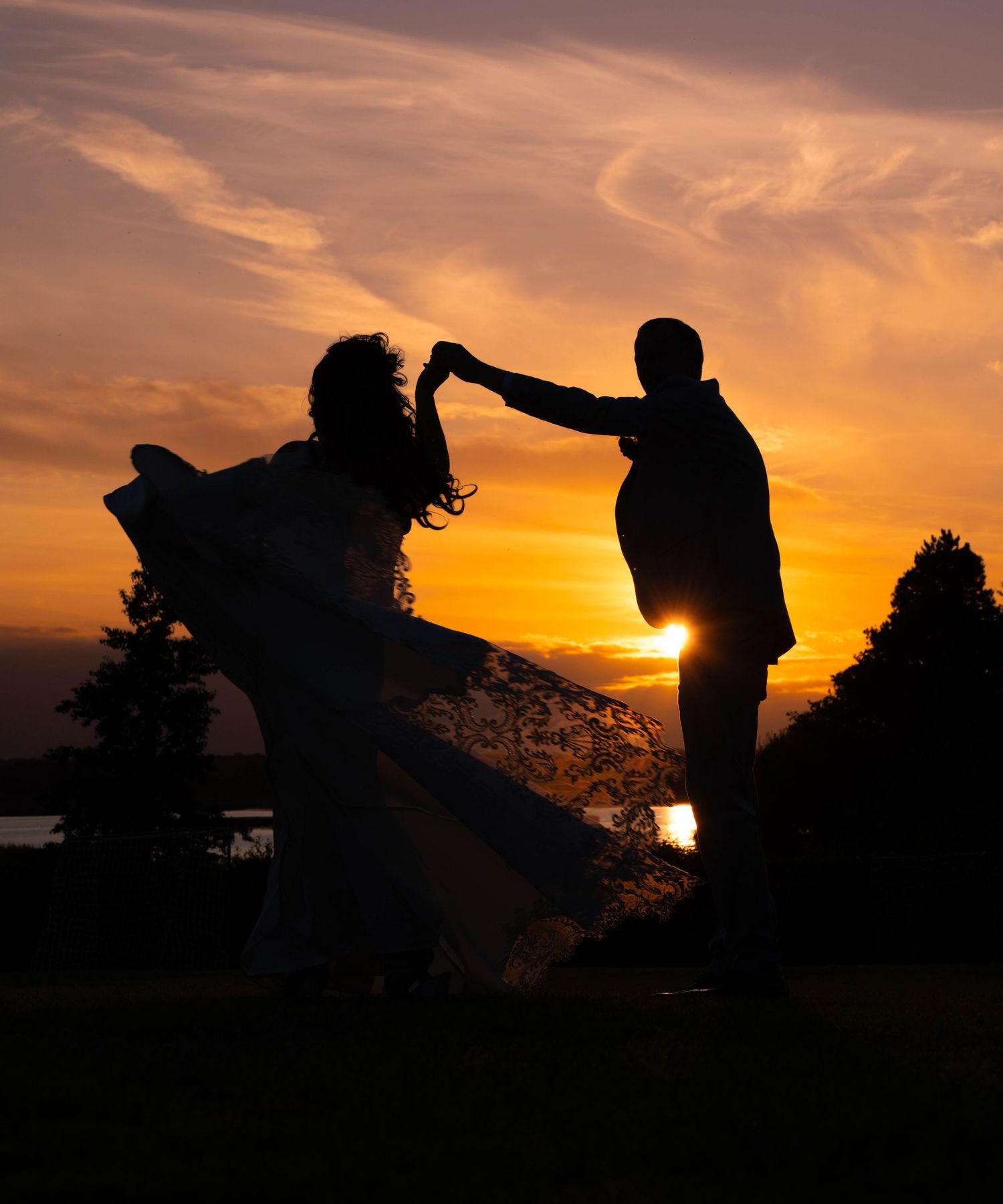 Couple dancing in silhouette against stunning golden sunset with flowing dress.