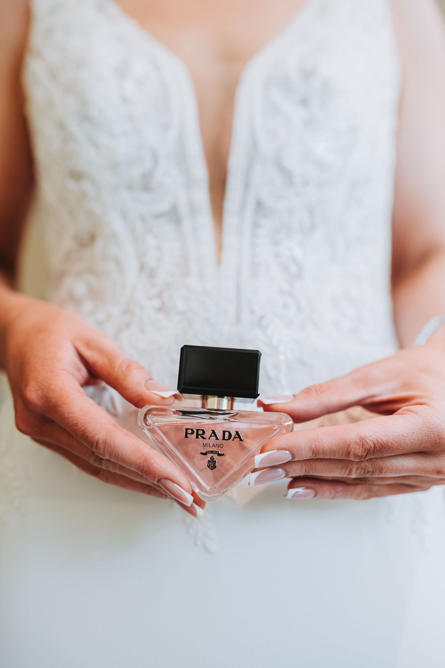 Close-up shots of hands holding a Prada perfume bottle against a white wedding dress.