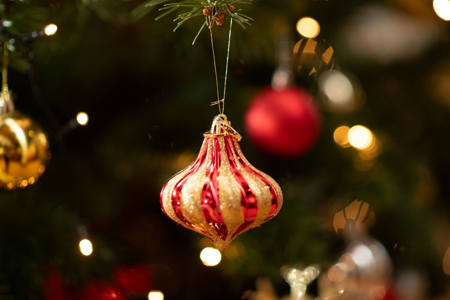 A vintage-style red and gold ornate glass Christmas ornament hangs on a tree with bokeh lights in the background.