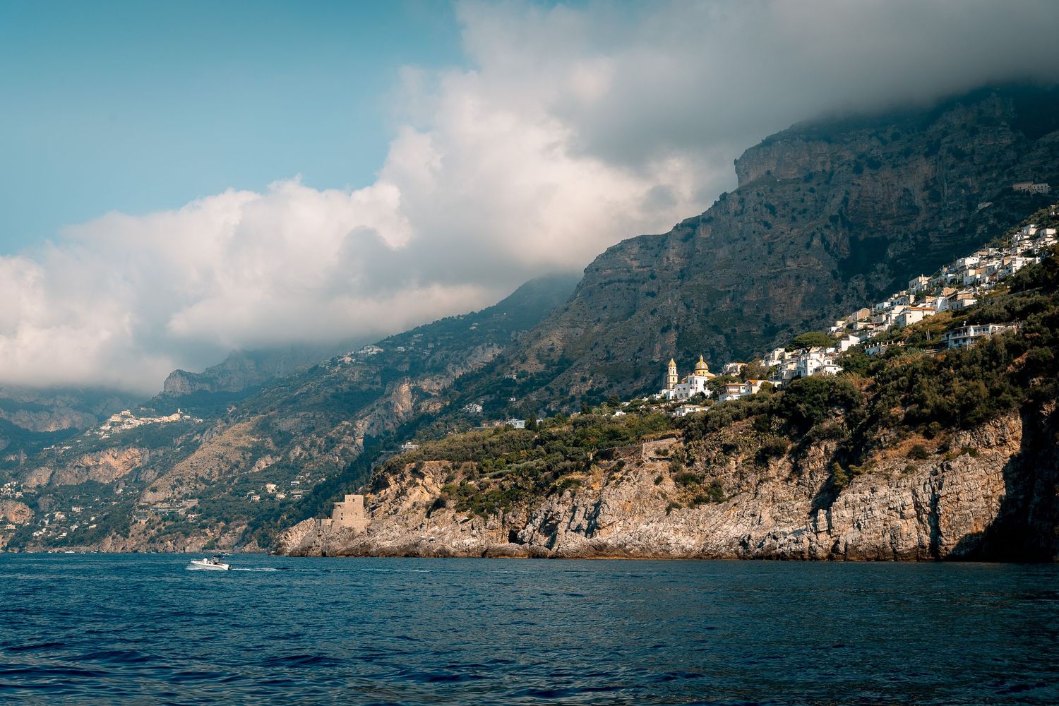 Dramatic Amalfi Coast cliffside village perched above deep blue Mediterranean waters under cloudy skies.