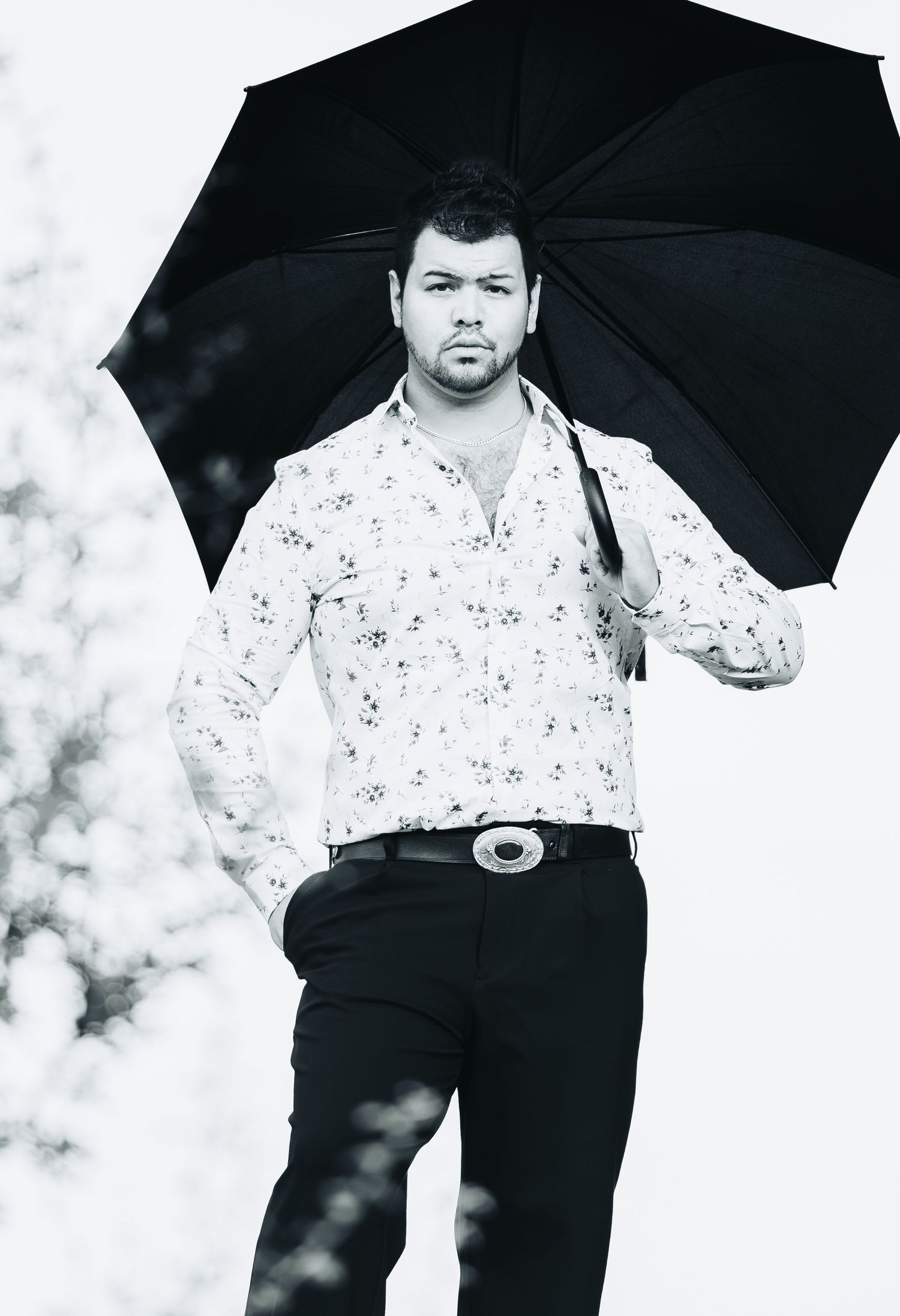 Man in floral shirt holding black umbrella outdoors in black and white photo.