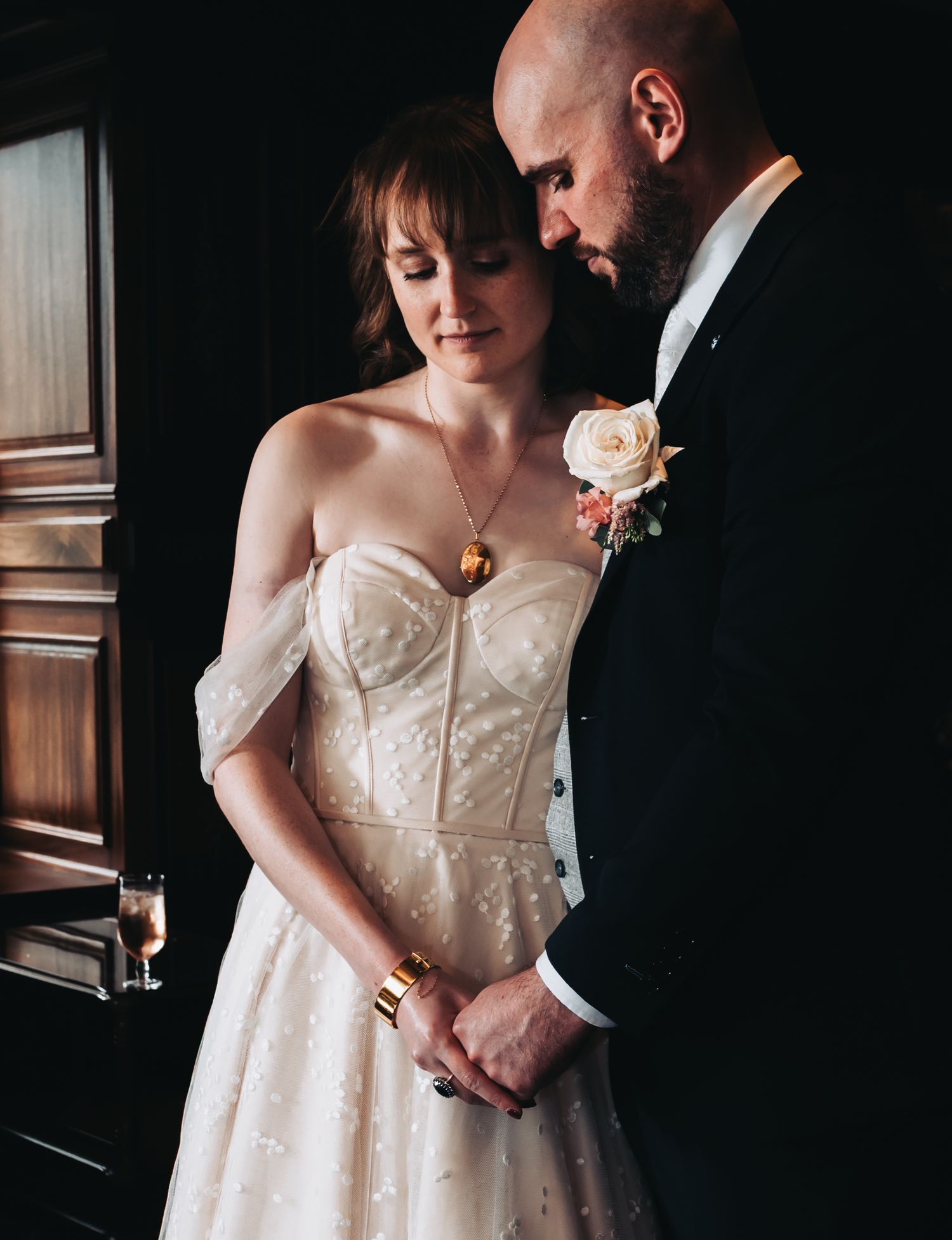 Bride in off-shoulder lace gown and groom in black tuxedo share an intimate moment at their wedding.