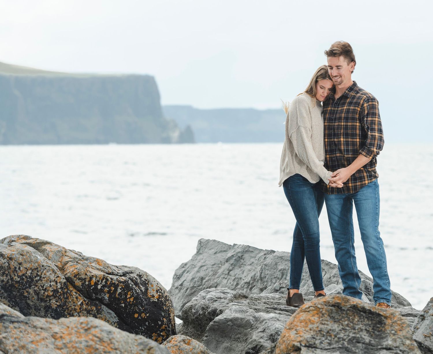 Couple standing on rocky coastal outcrop with ocean views.