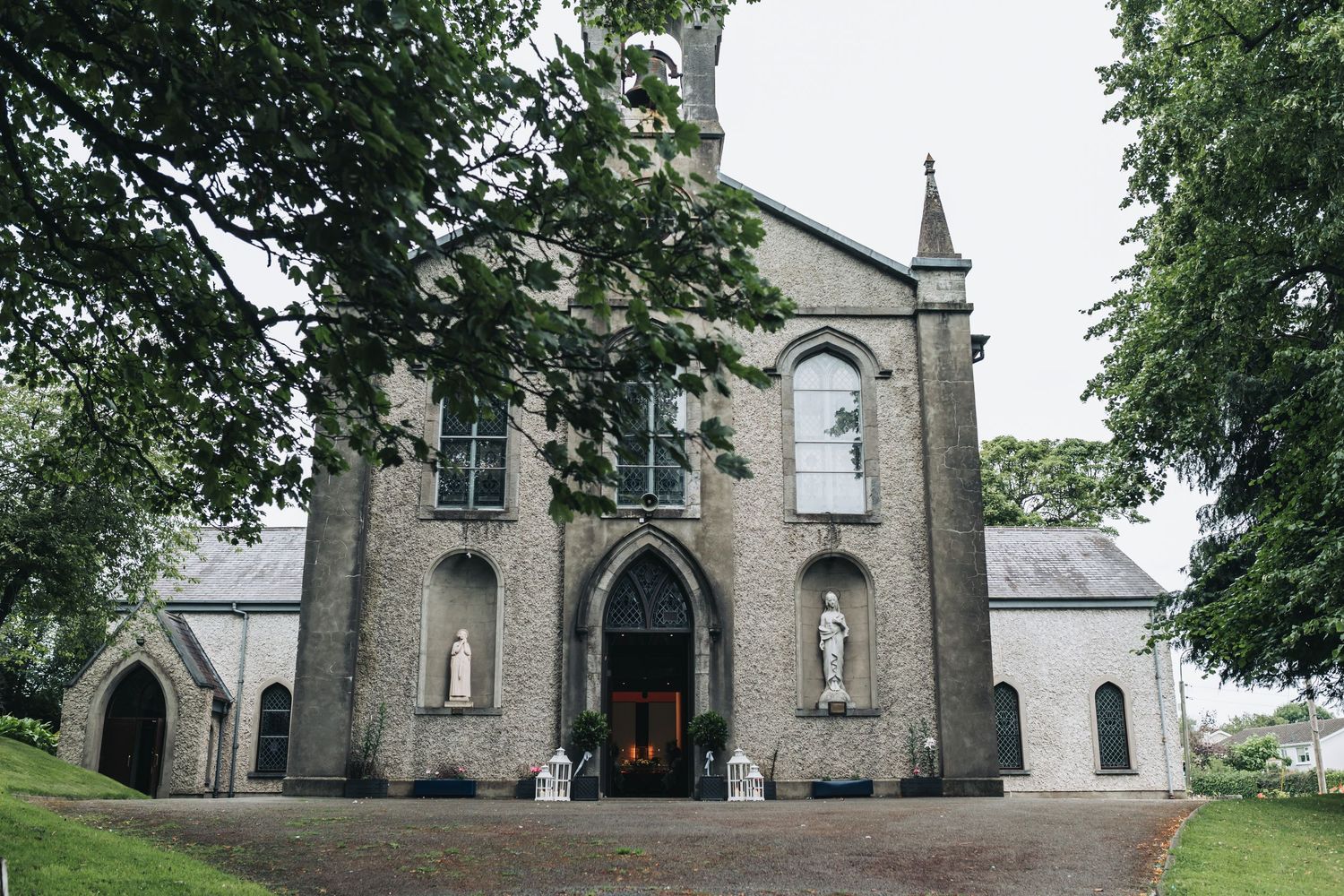 Gothic stone church with arched entrance, statues, and lush trees, perfect wedding ceremony venue.