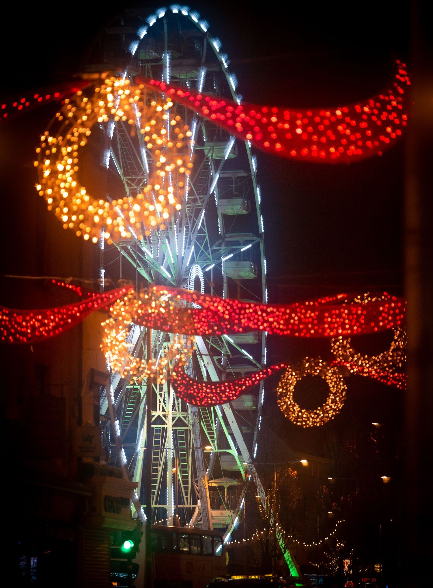 Colorful Ferris wheel illuminated at night surrounded by festive crescent moon and wreath decorations.