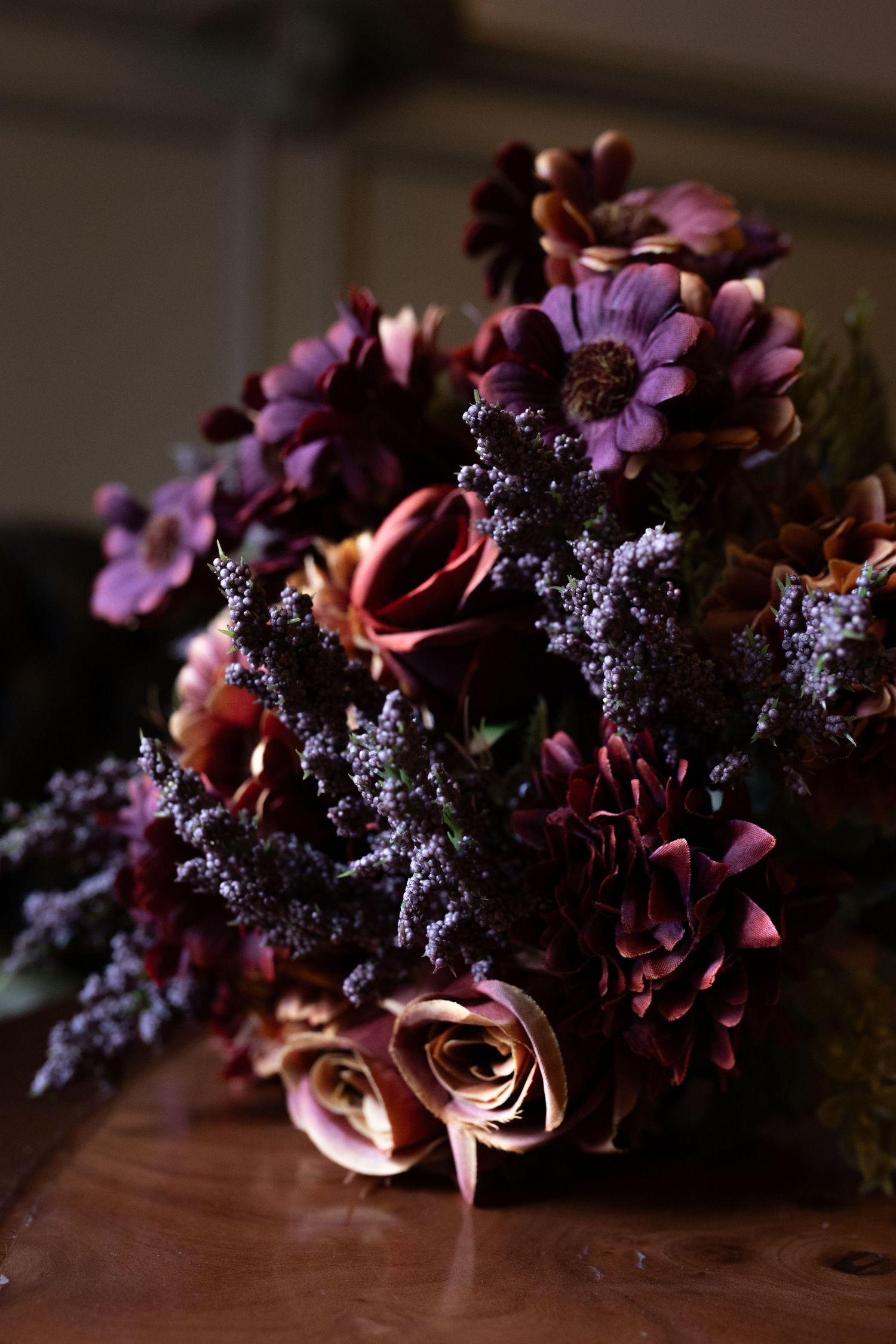 Dark and moody floral arrangement with purple blooms and dusky pink roses on wooden surface.