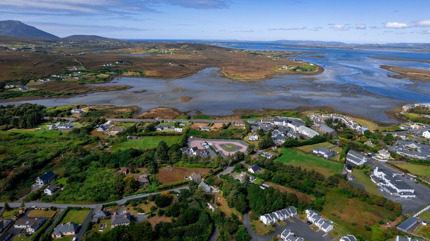 Aerial view of a coastal Irish village surrounded by tidal estuaries and mountain backdrop.