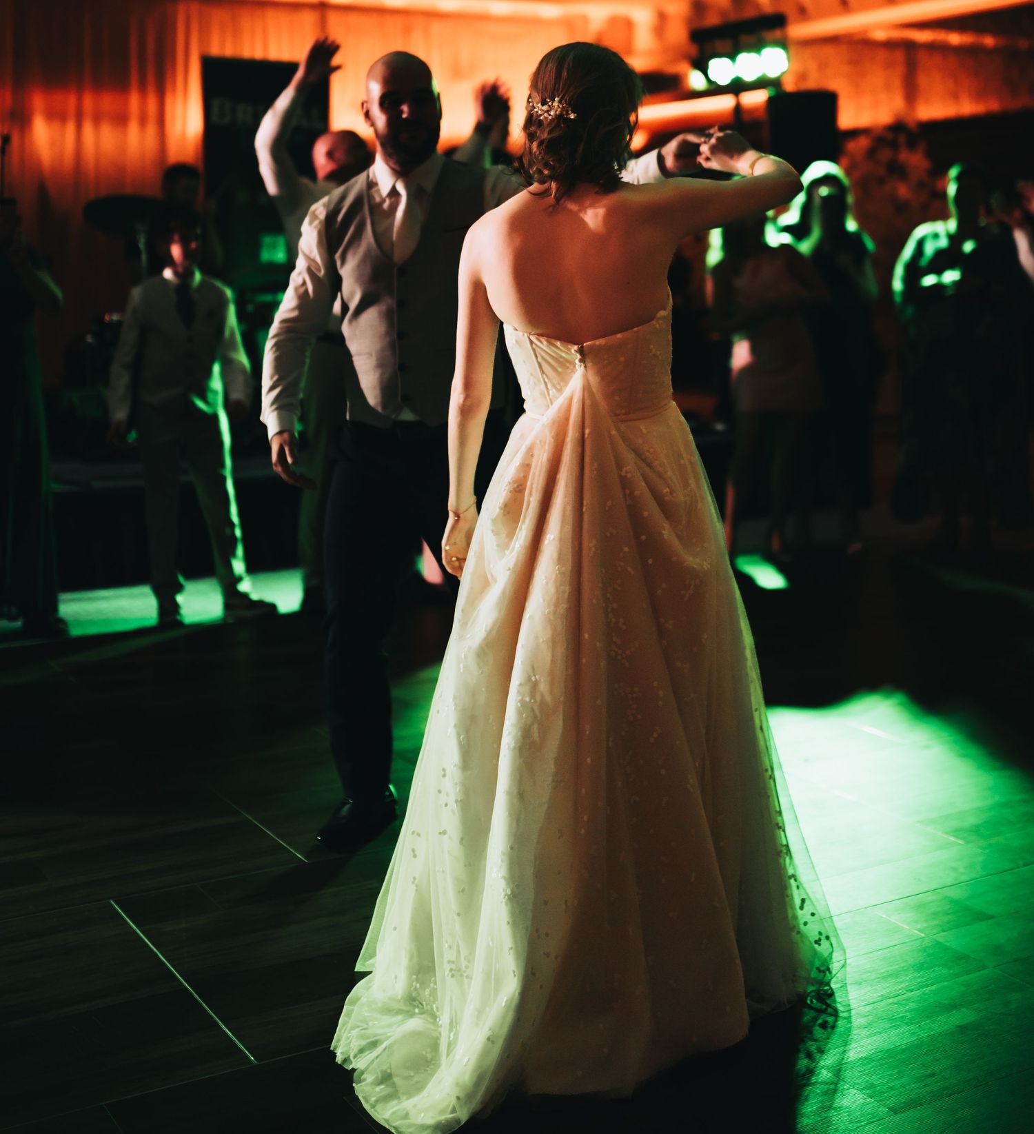 Bride in elegant white gown dancing with groom under green lights at wedding reception.
