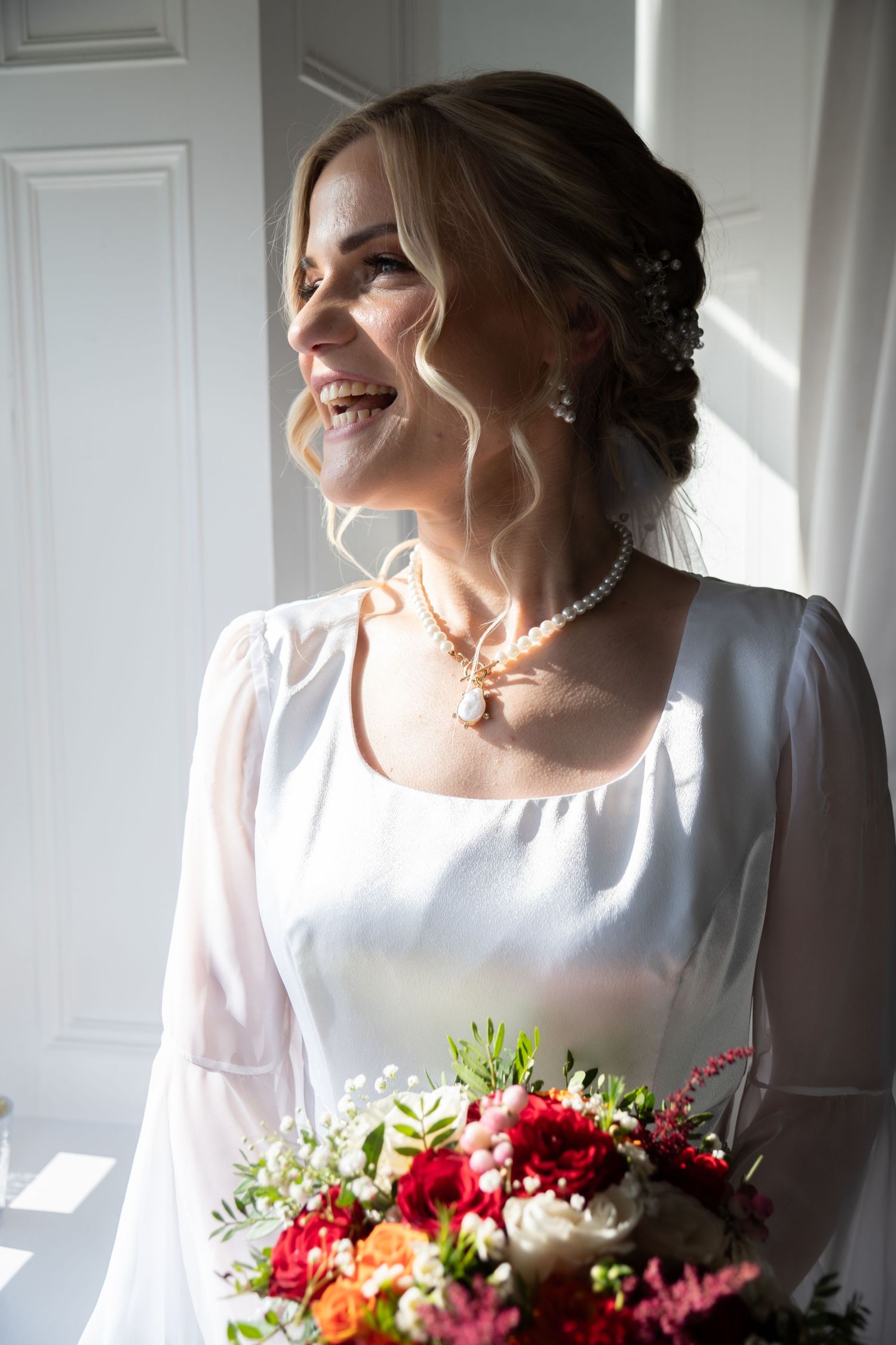 Sunlit portrait with a vibrant red and pink wedding bouquet.