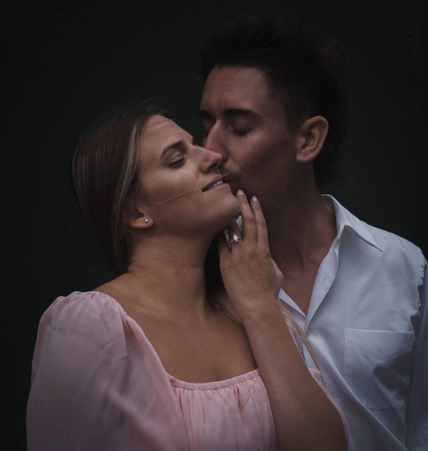An intimate portrait of a couple in soft lighting against a dark background.