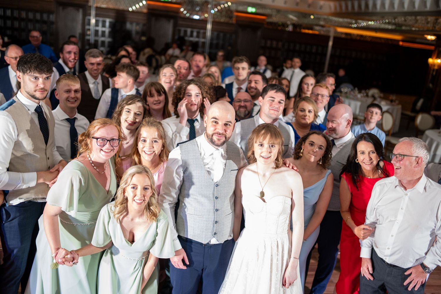 Large wedding party group photo with bride, groom, and guests in sage green and neutral attire.