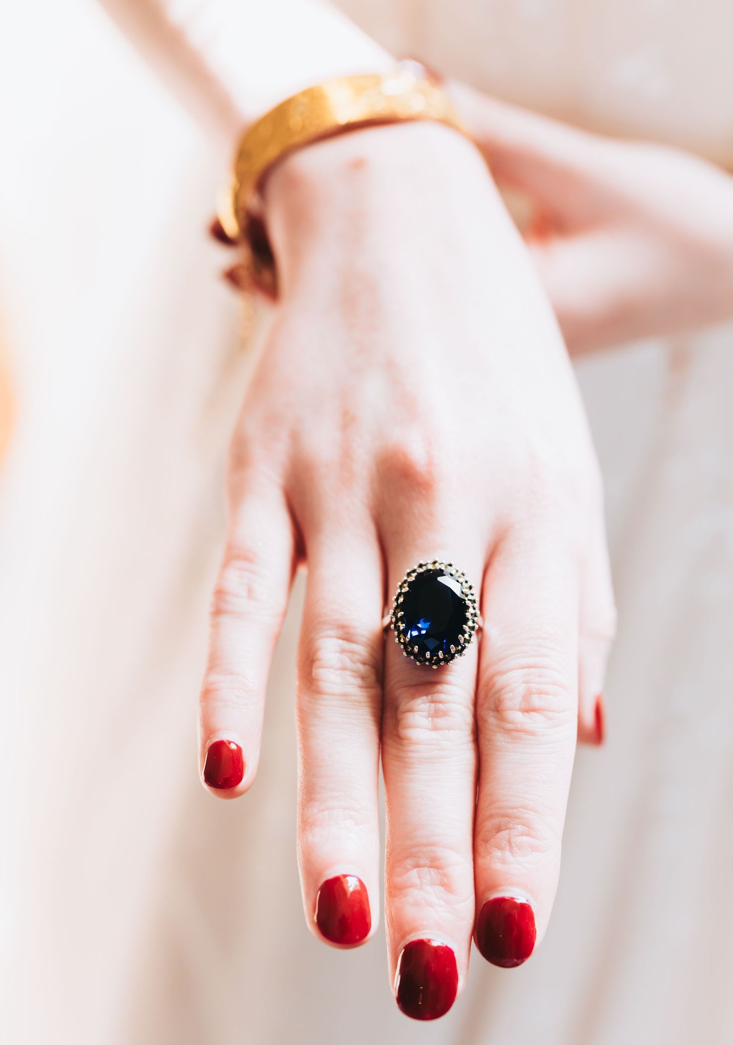 Bride wearing a dark oval gemstone ring with decorative band and gold bangle bracelet with red manicure.