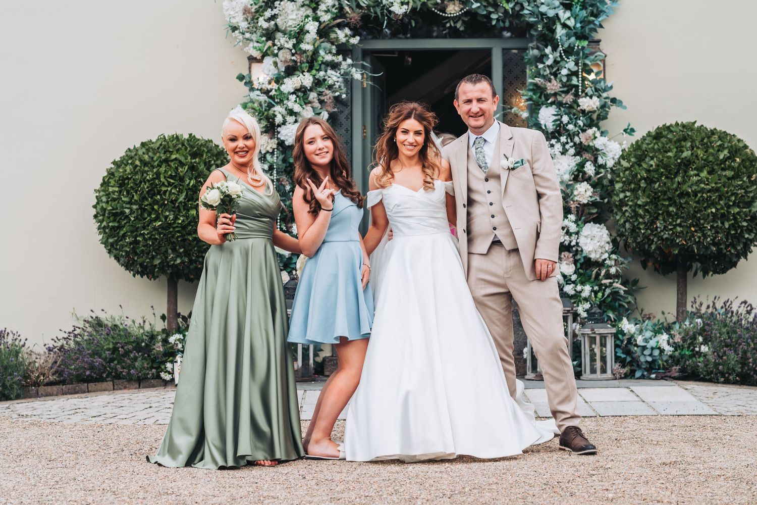 Wedding party group photo featuring bride in white gown with family members in sage green and beige attire.