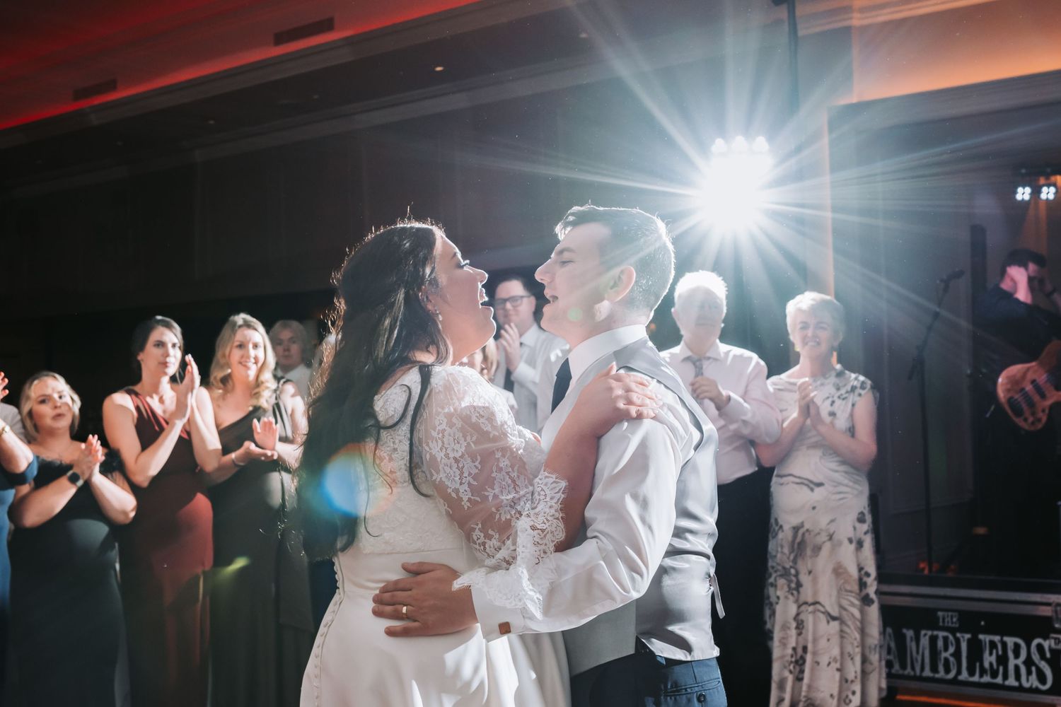Bride and groom share their first dance at wedding reception while guests applaud in elegant ballroom.