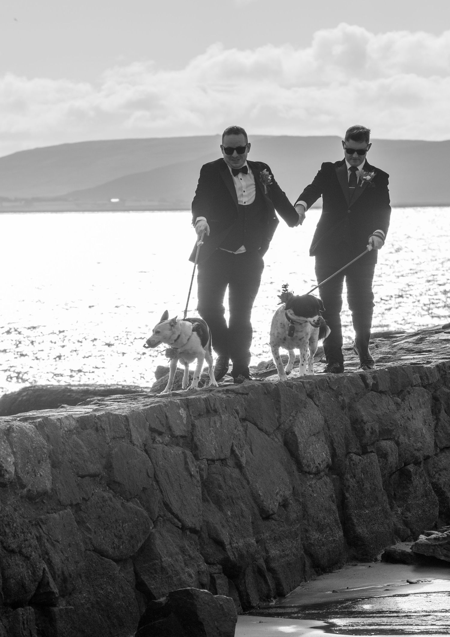 A couple walking their dogs along a rocky coastal path in dramatic black and white.