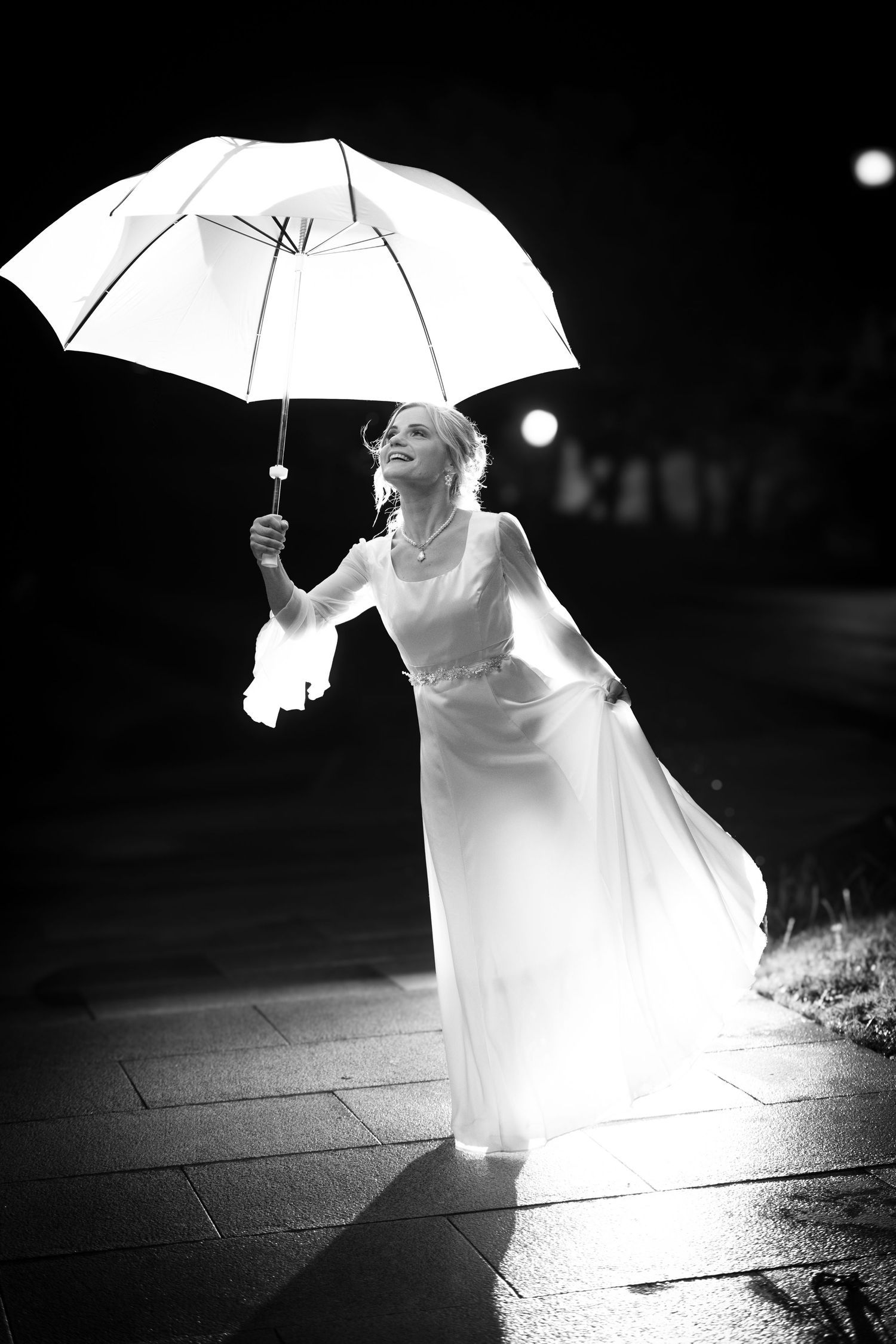 Dramatic black and white photo of a bride with a white umbrella at night.