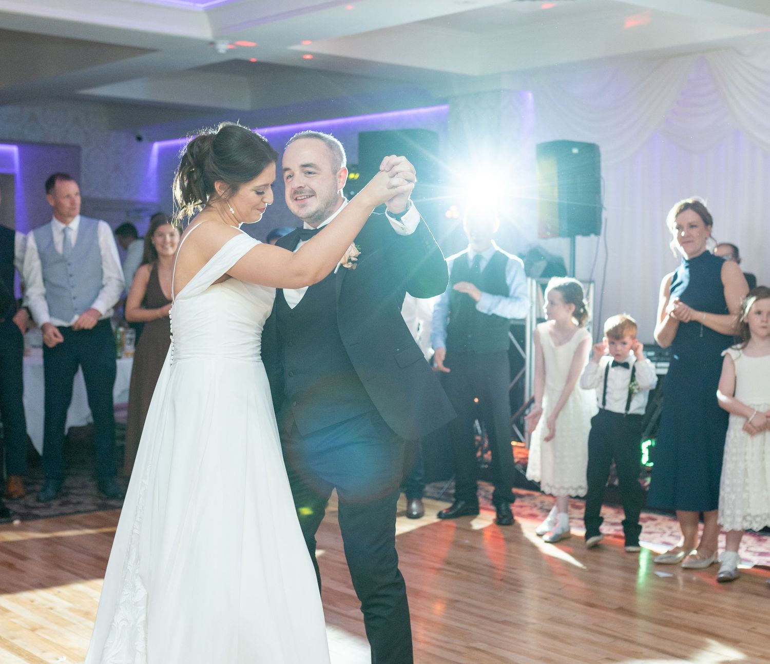 Bride and groom share first dance at wedding reception while guests watch and celebrate around them.