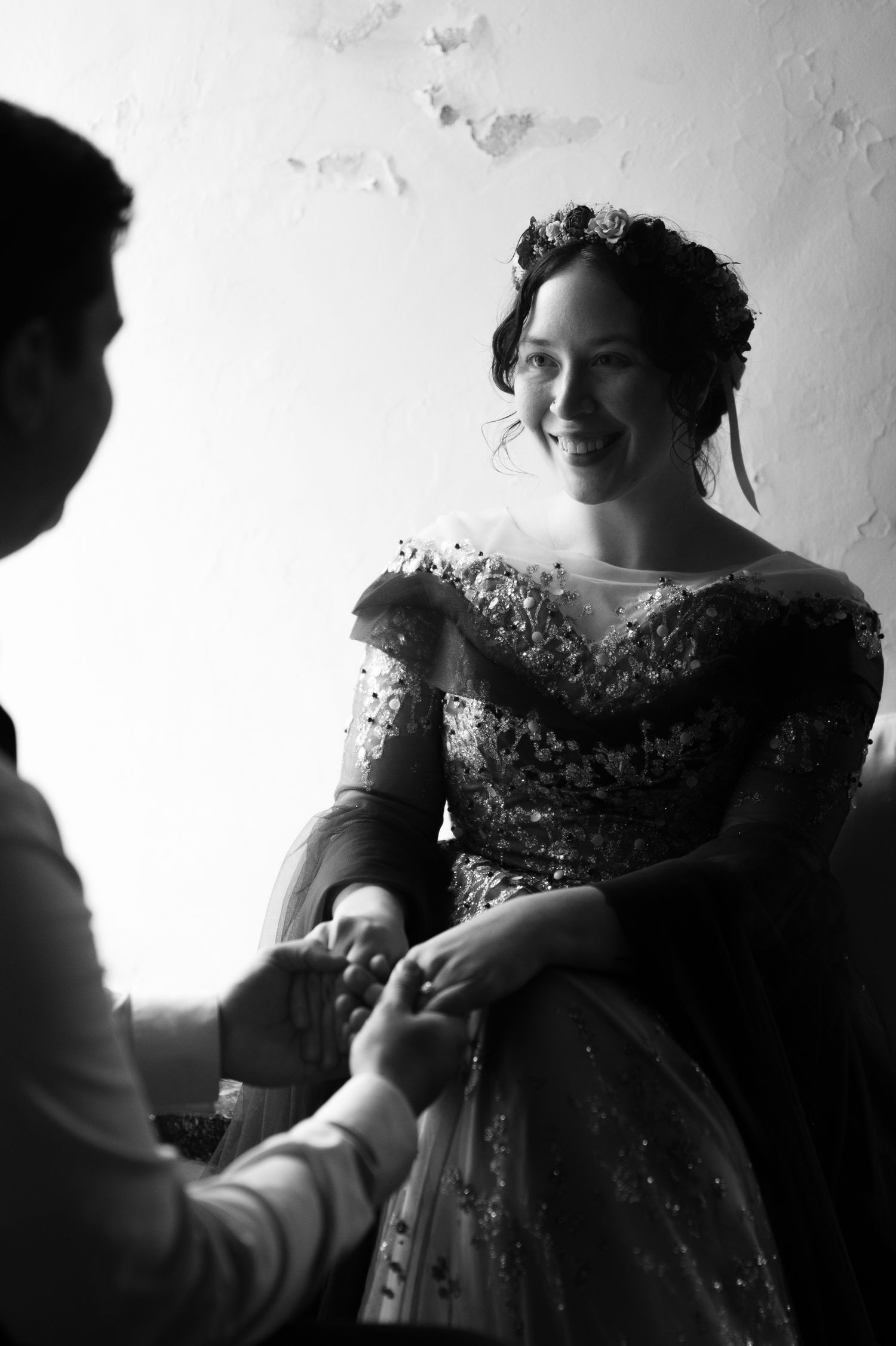 Smiling bride in embellished off-shoulder gown holds hands with groom in black and white wedding photo.