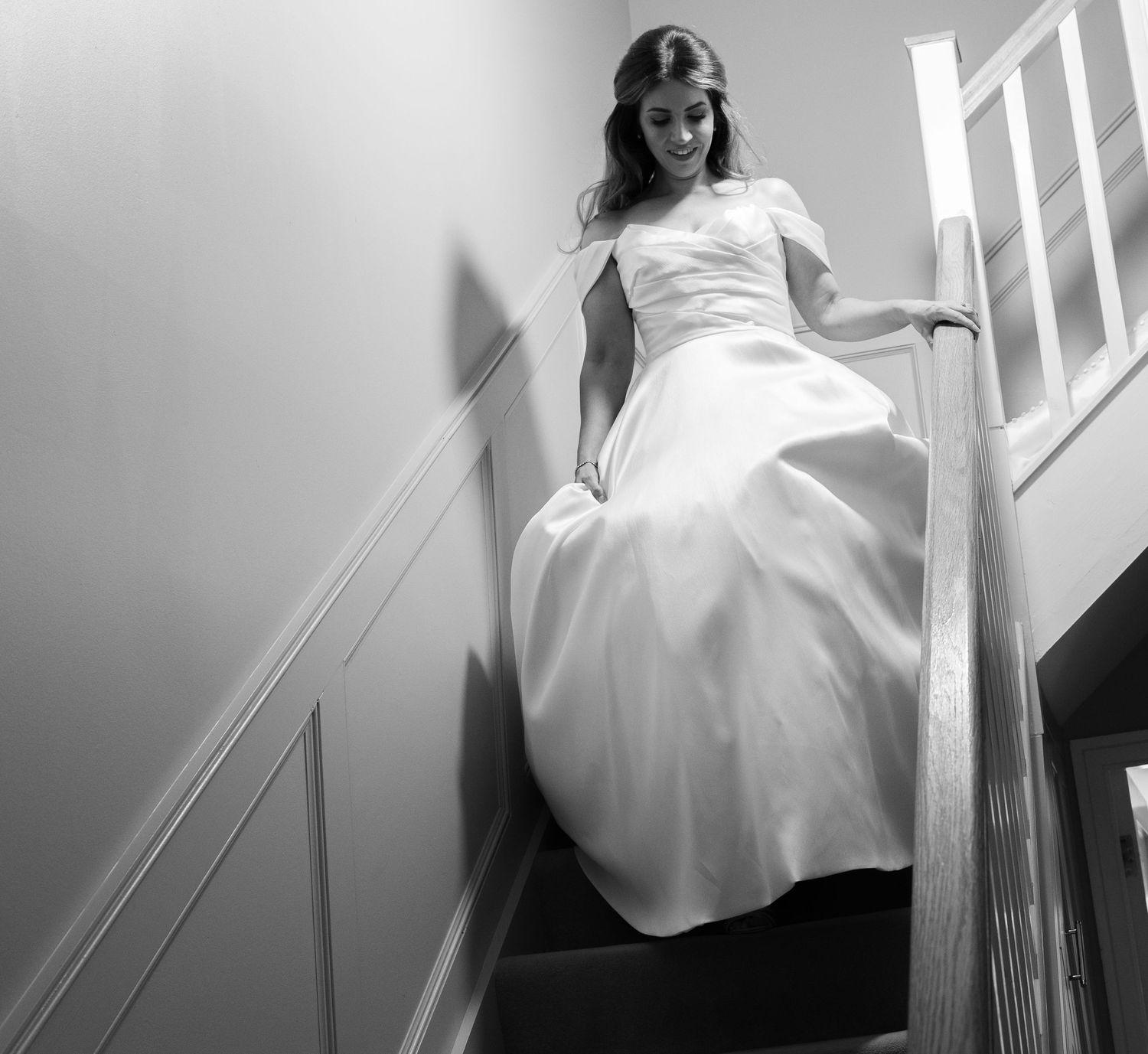 Bride in white wedding gown descending staircase in black and white photo.