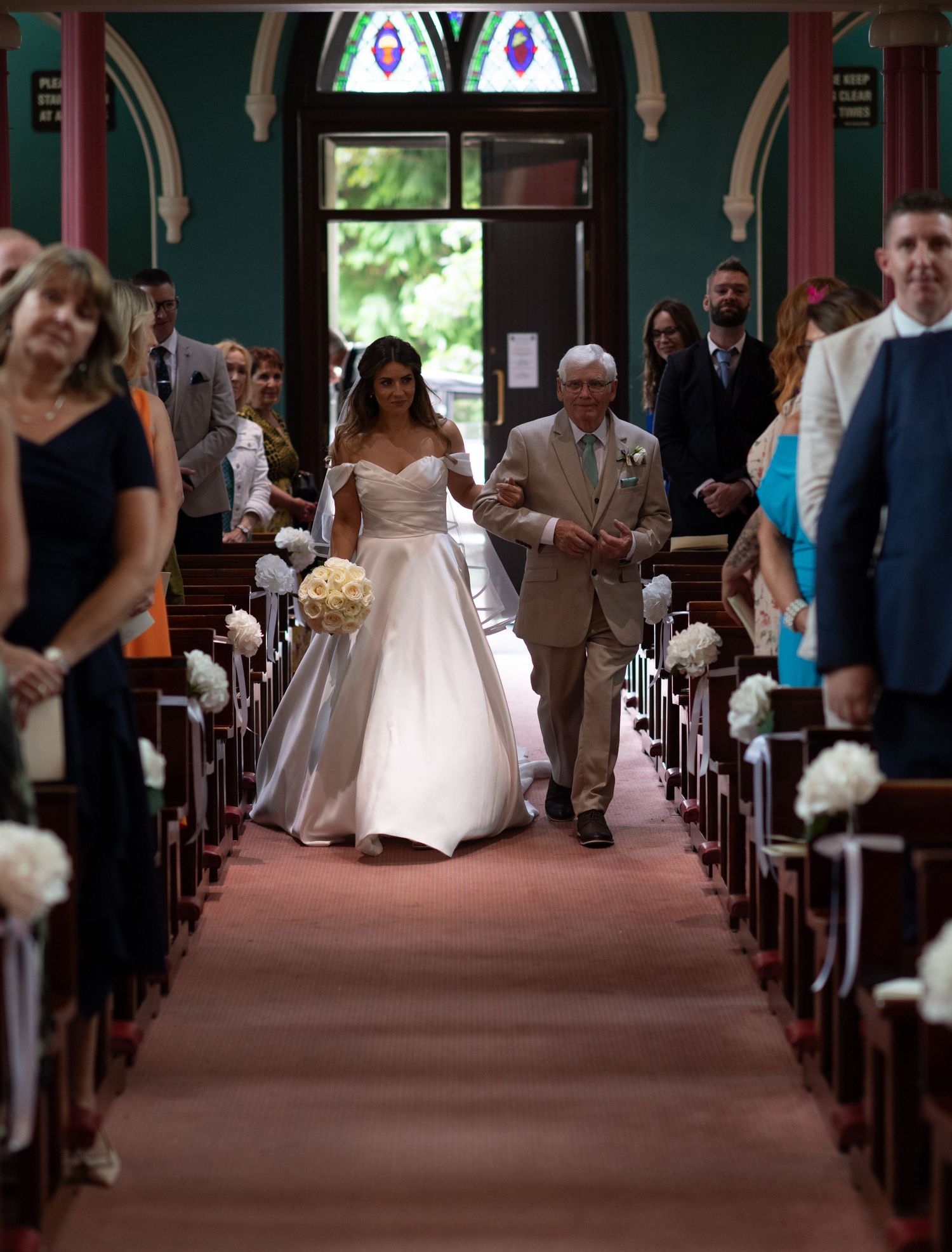 A bride walks down the church aisle escorted by her father during a traditional wedding ceremony.
