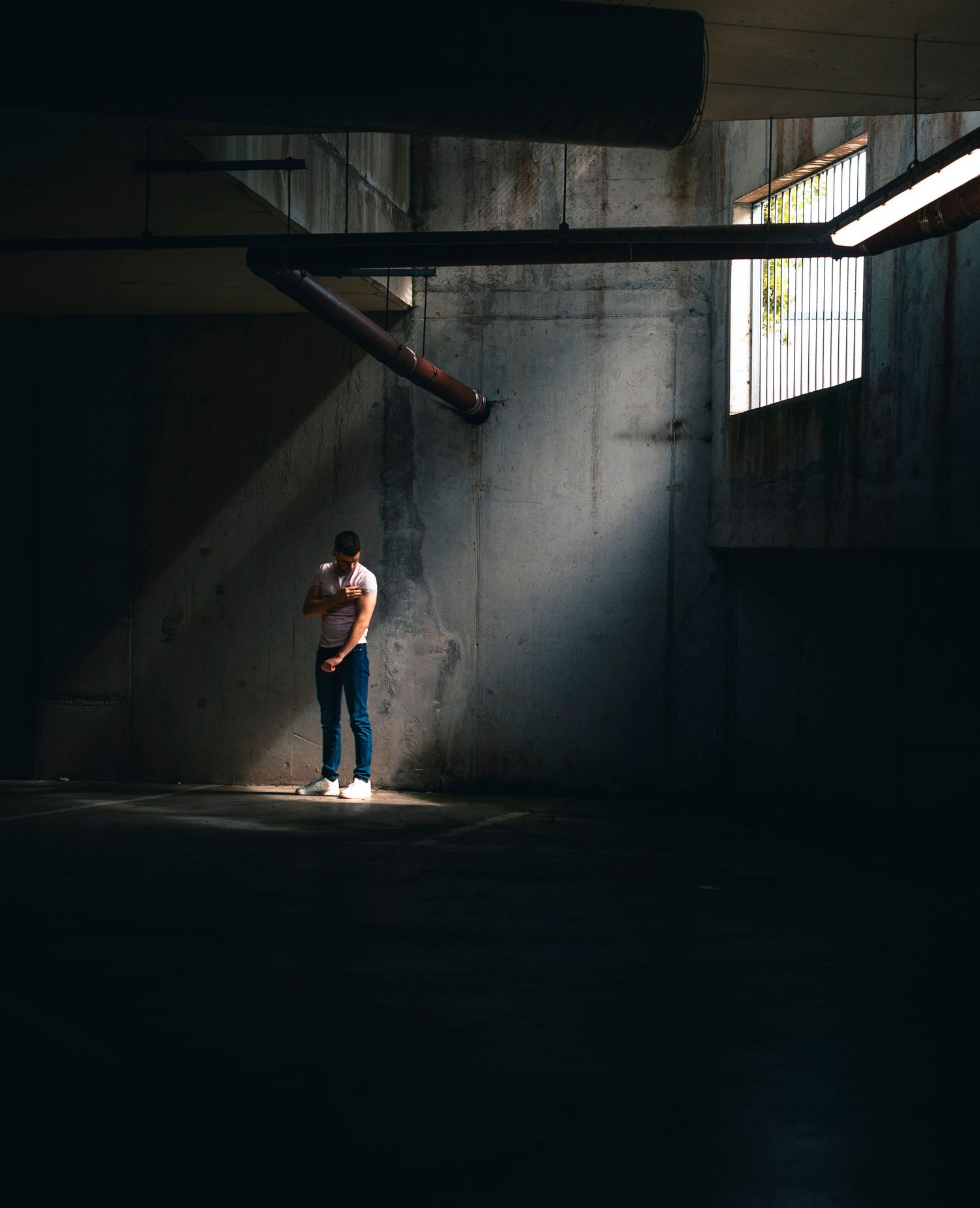 Person standing alone in a dramatic shaft of light inside a dark concrete parking garage or industrial building.