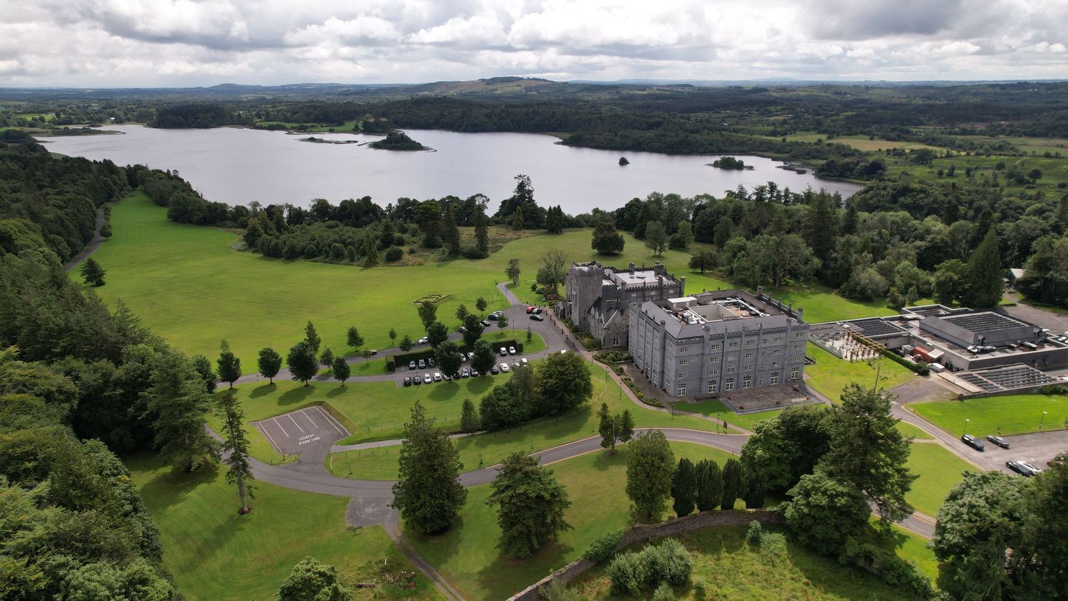 Bird's eye view of luxury hotel property nestled between lake and rolling green hills.