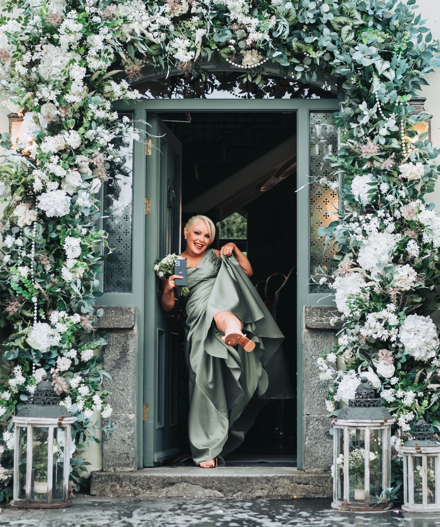 Wedding party jumps playfully in front of a floral-decorated entrance.