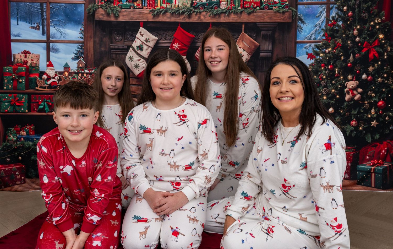 A group wearing matching red and white holiday pajamas poses together in front of a decorated Christmas backdrop.