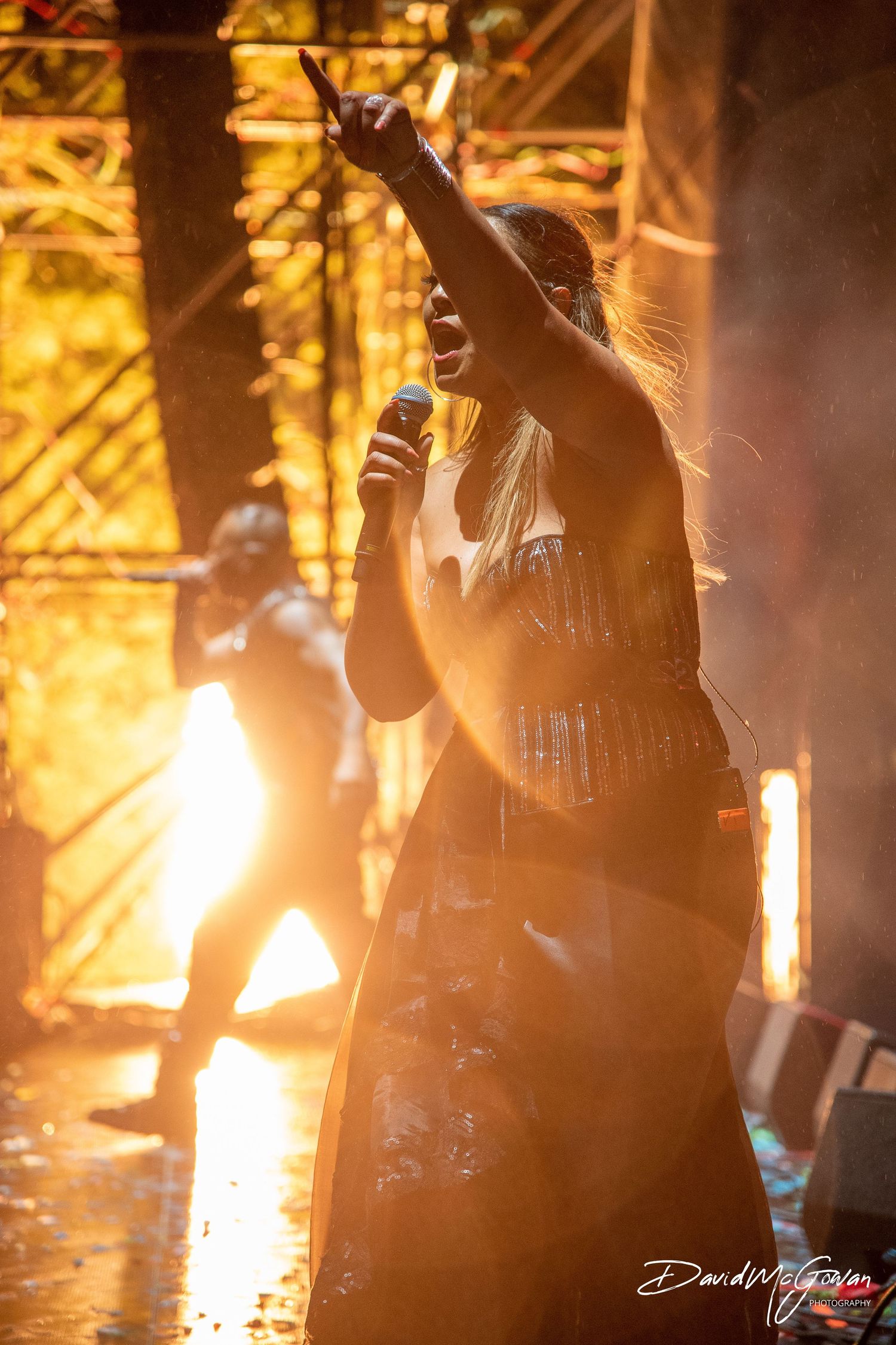 Silhouetted musicians perform on stage with dramatic orange lighting and smoke effects creating an atmospheric concert scene.