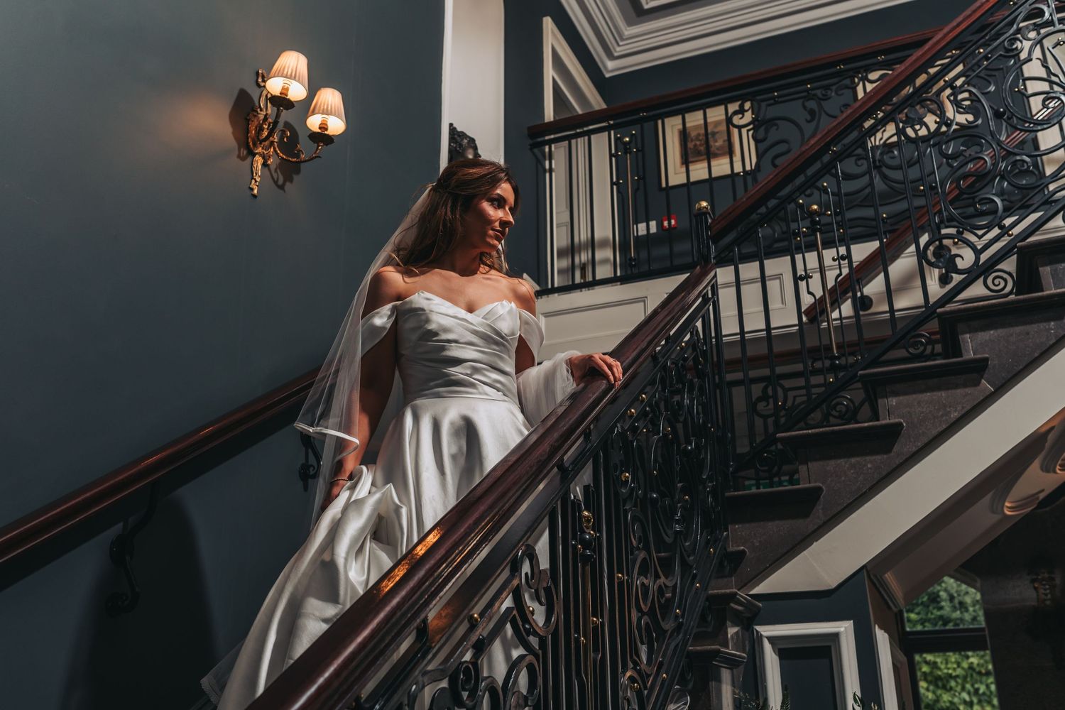 Wedding dress flowing down an elegant staircase with ornate iron railings.