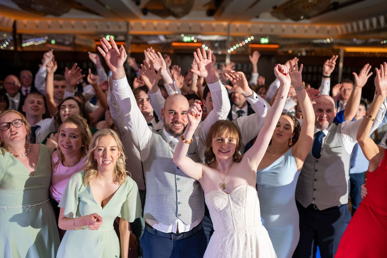 Wedding reception guests with raised arms celebrating on a dance floor.