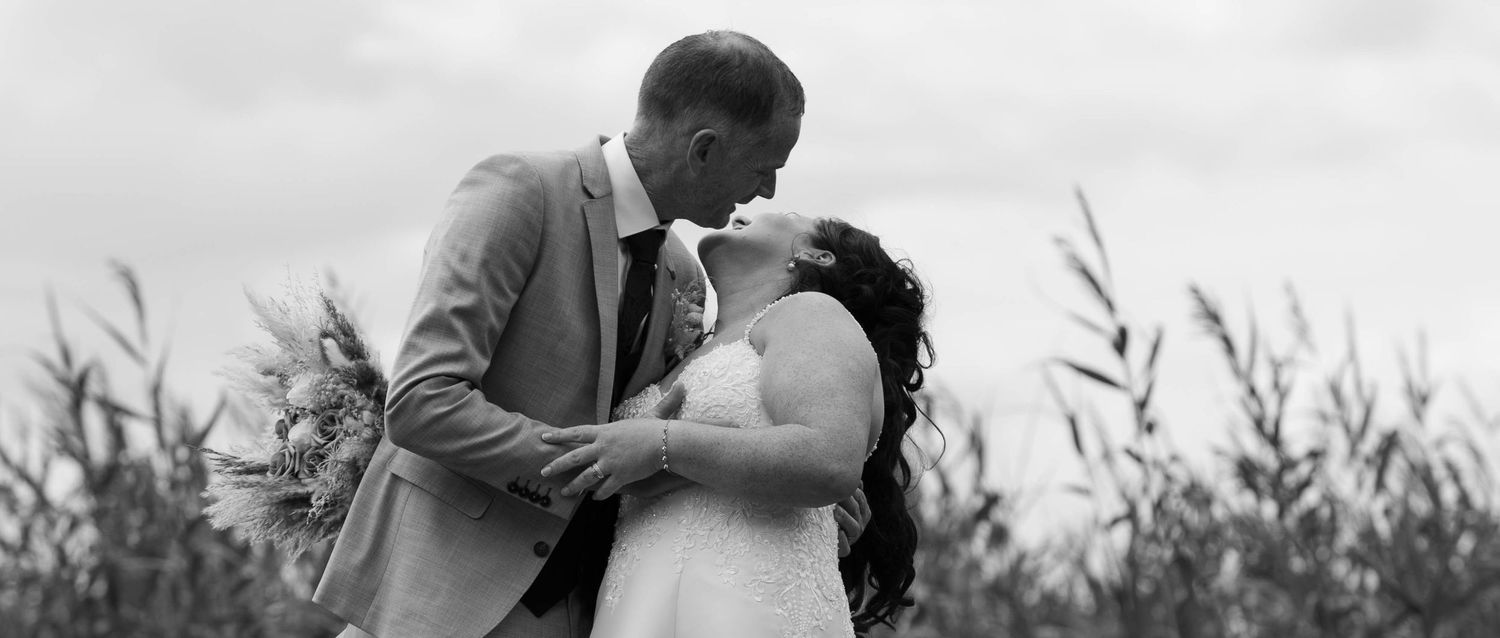 Black and white photo of bride and groom sharing tender kiss in field.