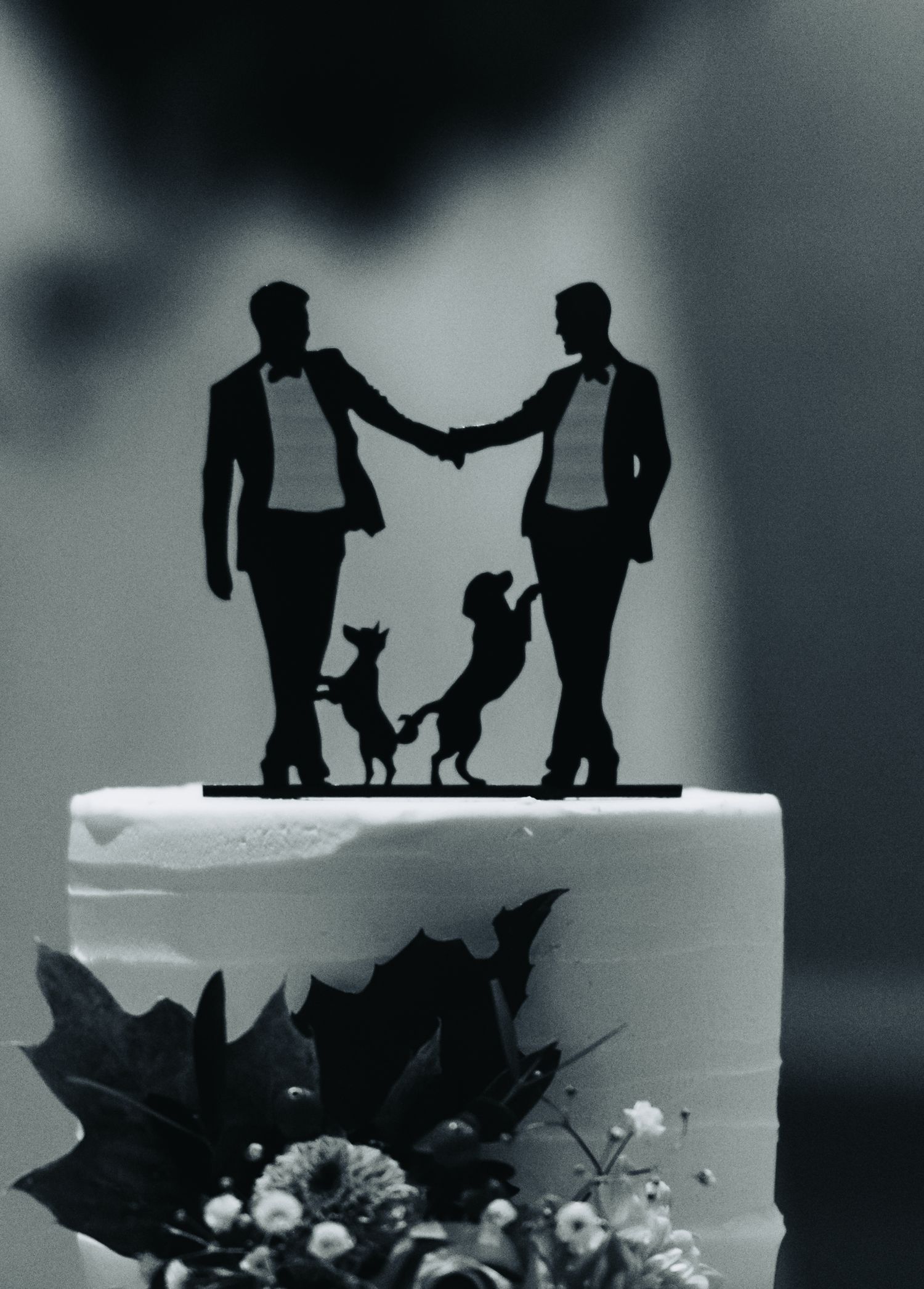 Wedding cake topper silhouette featuring a couple and their pets in black against white frosting.