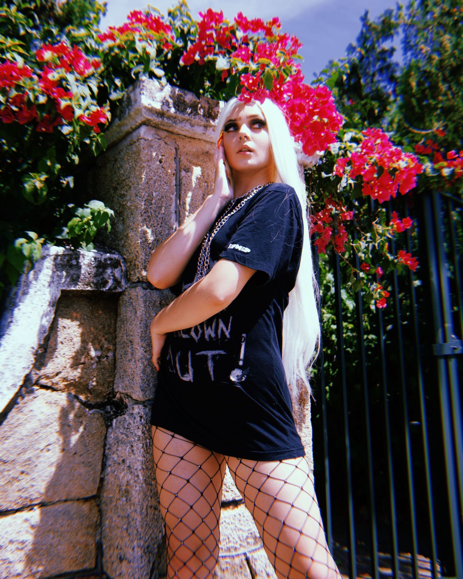 Fashion shoot featuring black outfit and fishnet stockings against red flowering bushes.