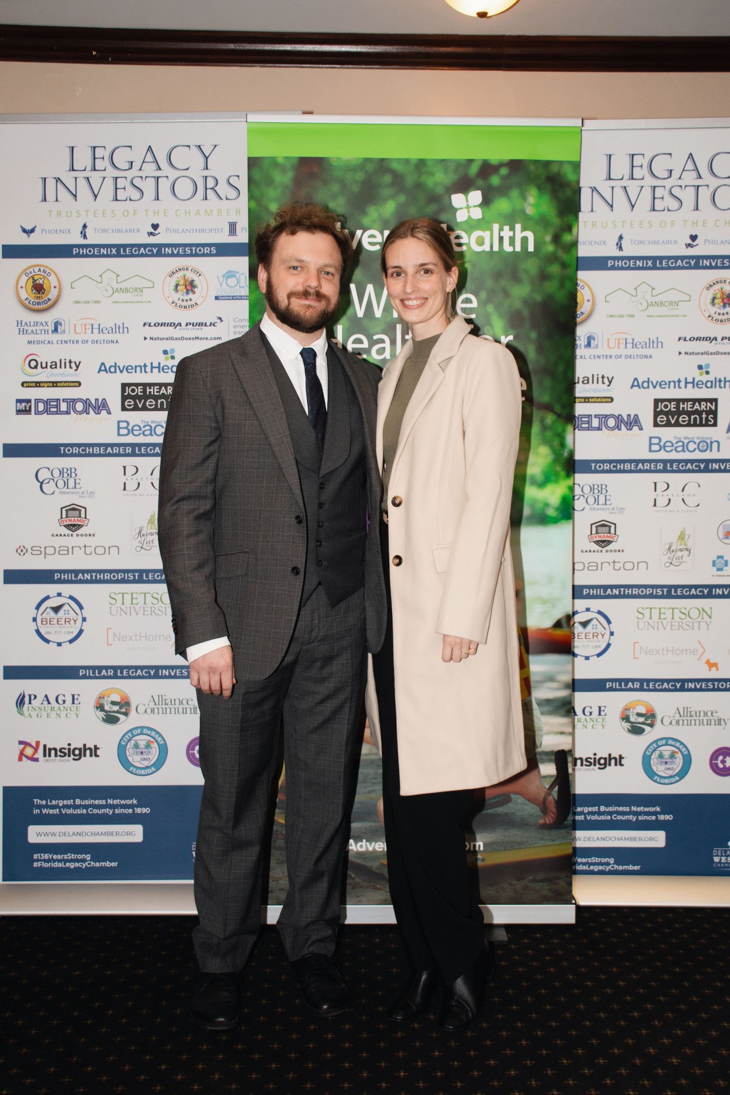 Two people stand in front of a corporate event backdrop with Legacy Investors branding and logos.