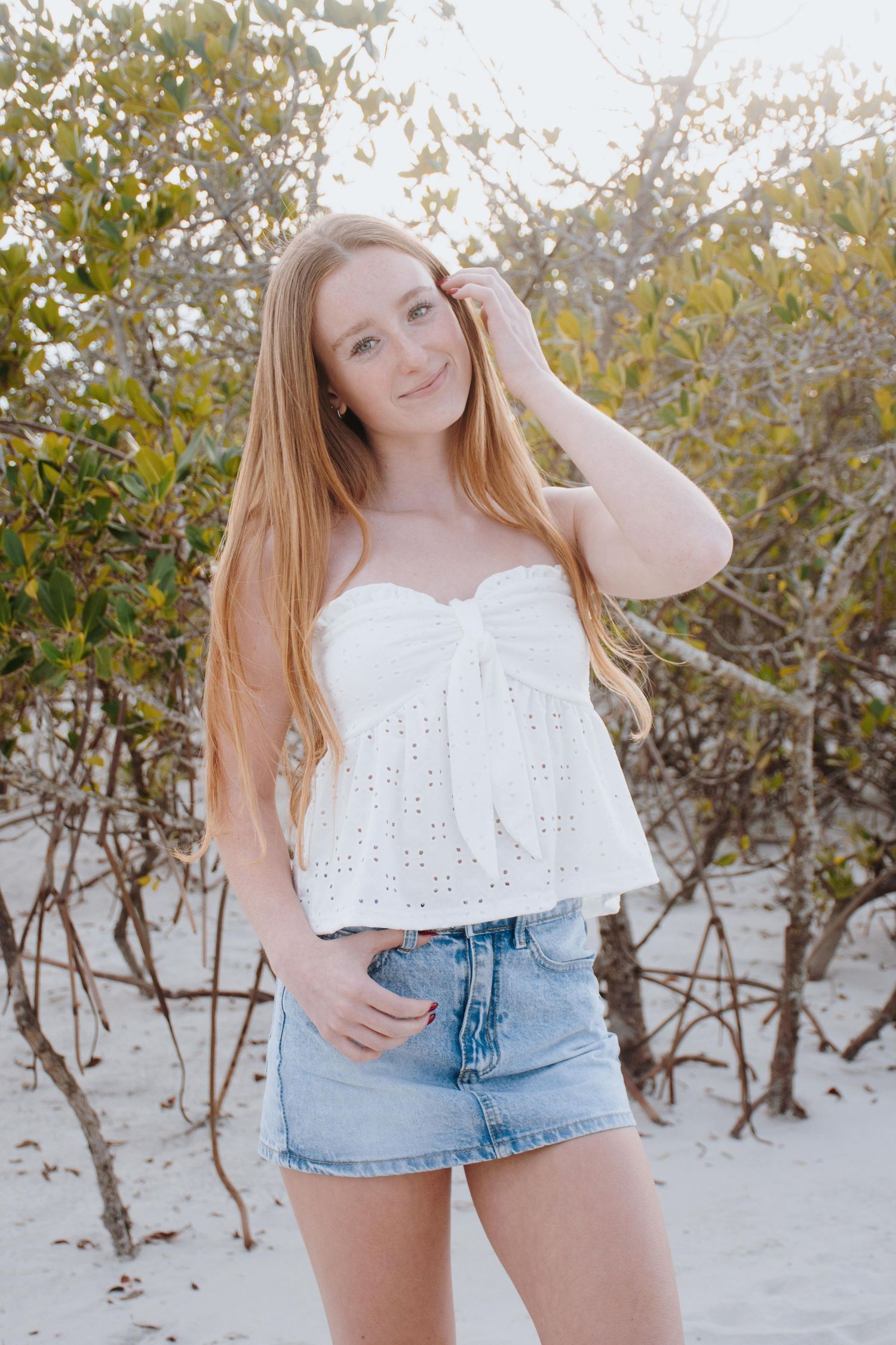 A casual summer photoshoot featuring white eyelet top and denim shorts against a beach backdrop.