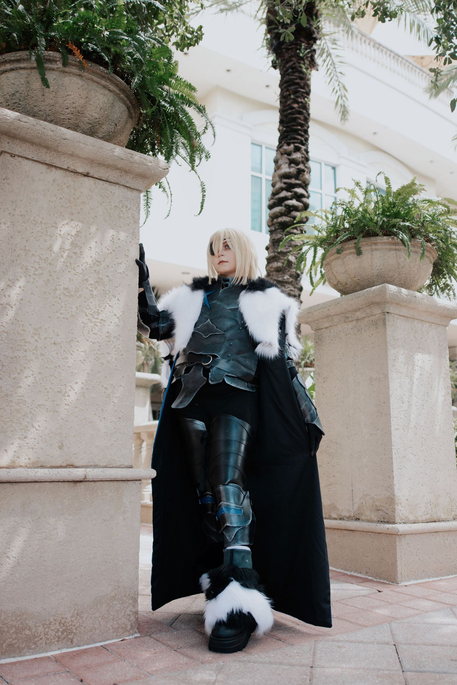 Dark fantasy cosplay featuring black armor and white fur trim photographed against stone architecture.