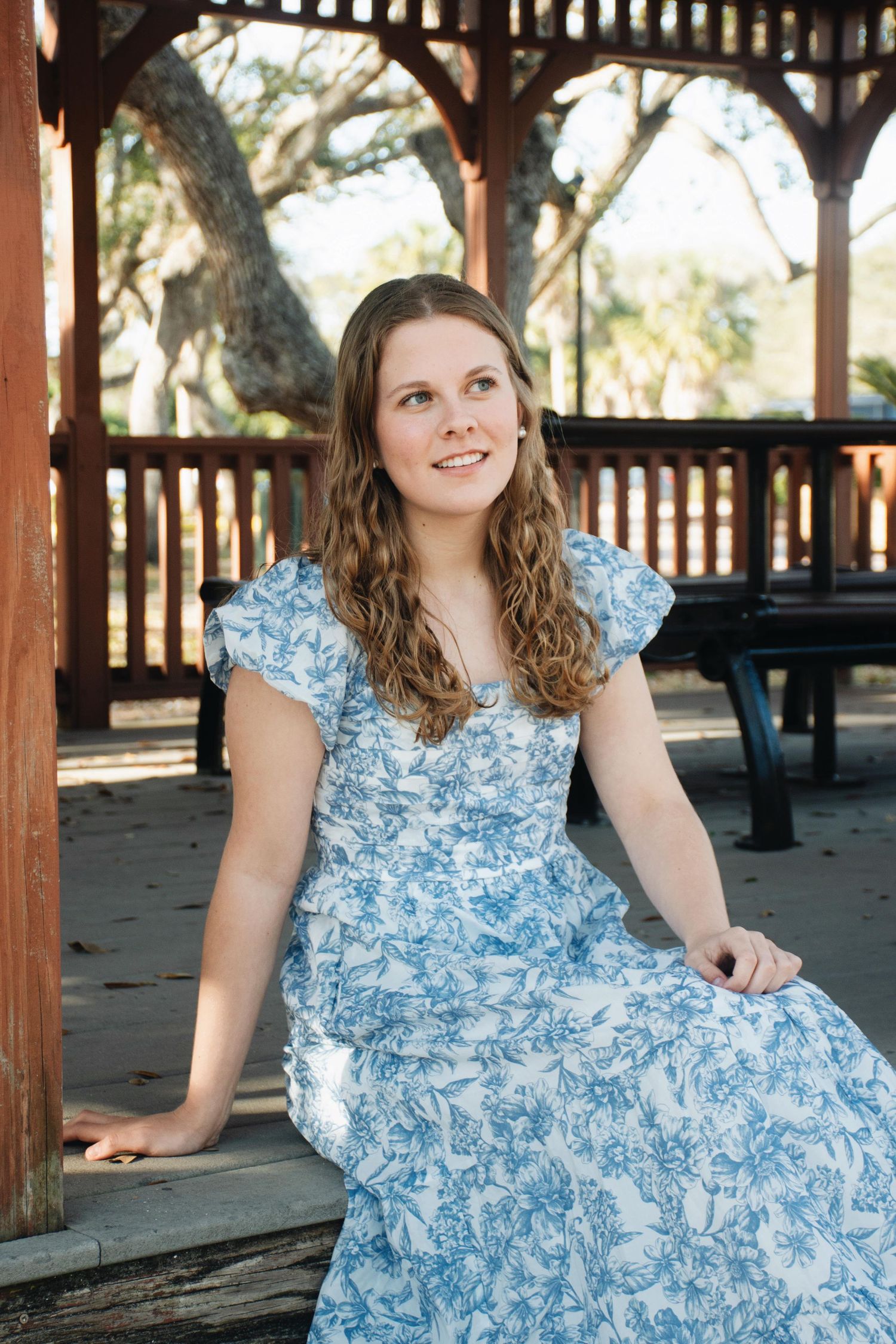A series of photos showing someone in a light blue floral dress sitting on wooden benches in an outdoor pavilion.