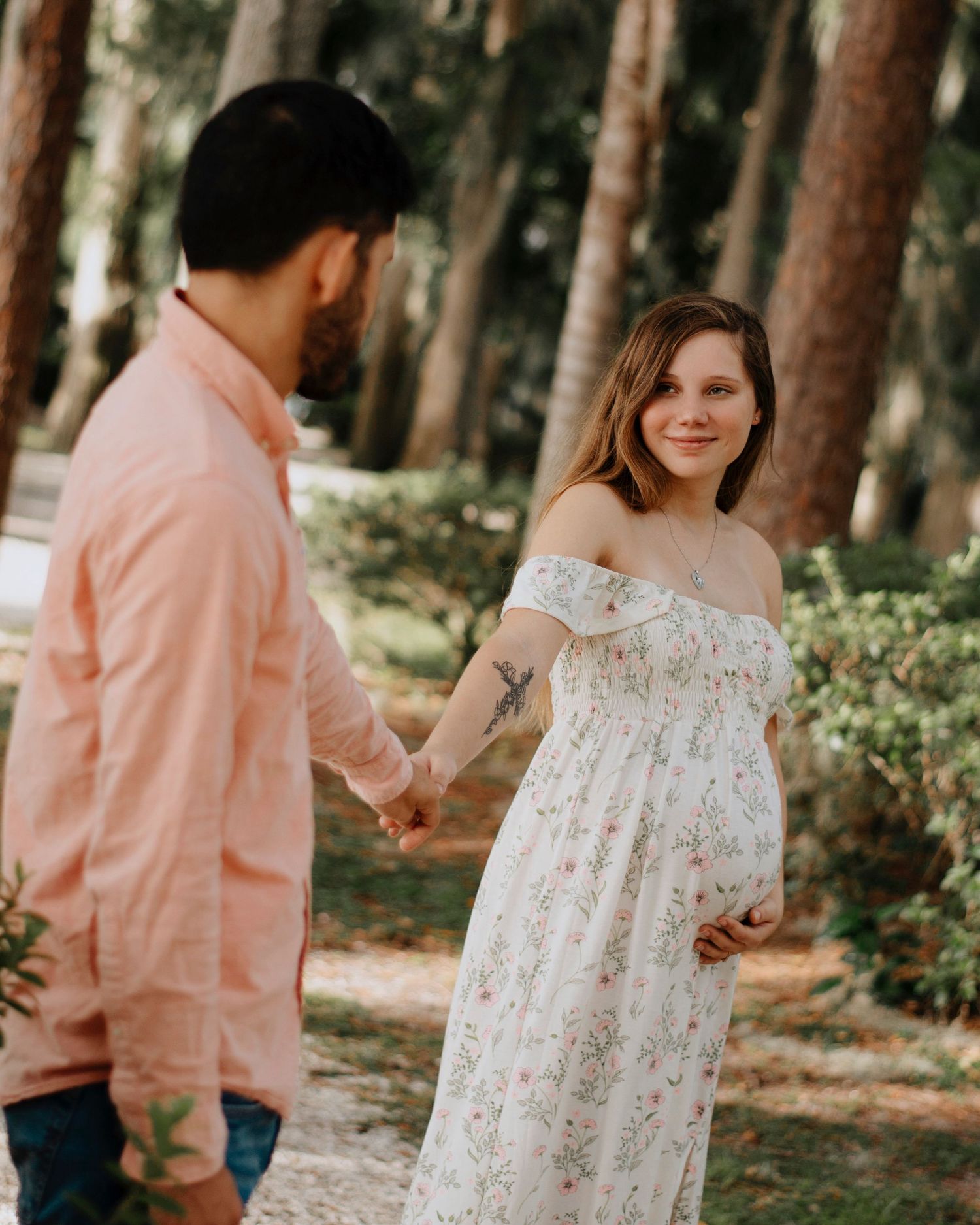 Romantic couple photoshoot in pink and white outfits among pine trees.
