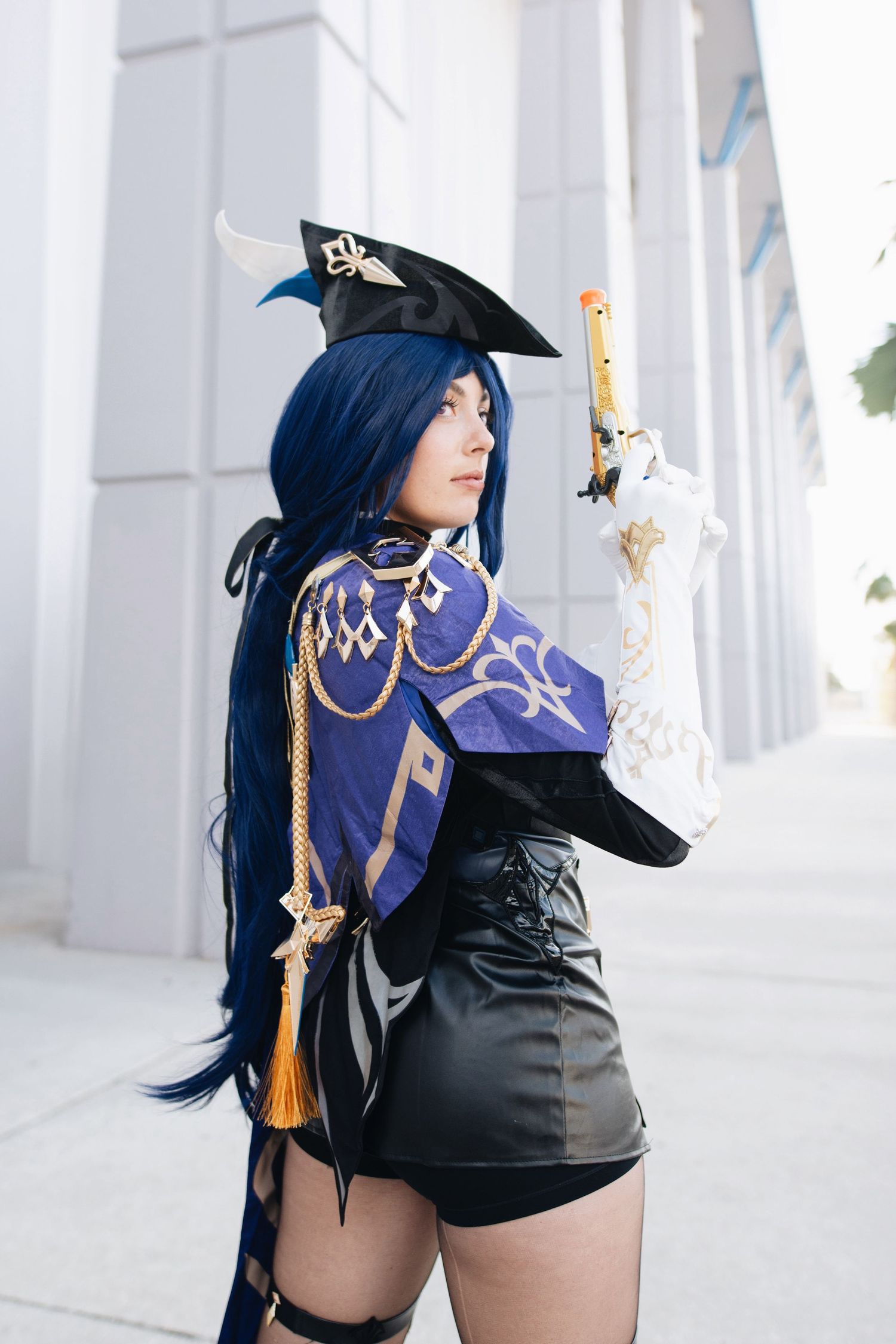 Cosplayer wearing a blue cape and black outfit poses between white pillars.
