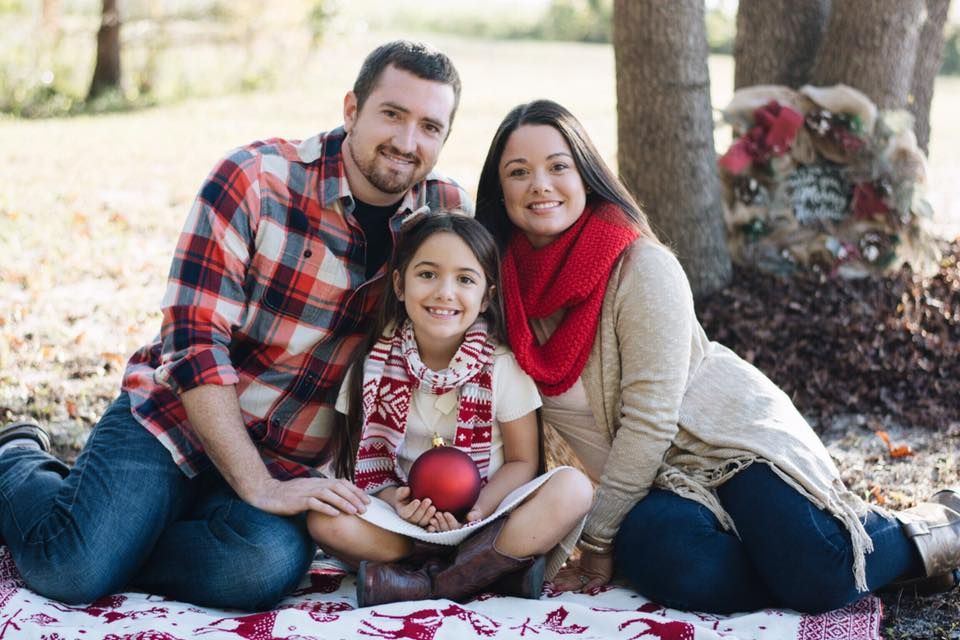 A family in coordinating red and plaid outfits sits together on a blanket outdoors during an autumn photoshoot.