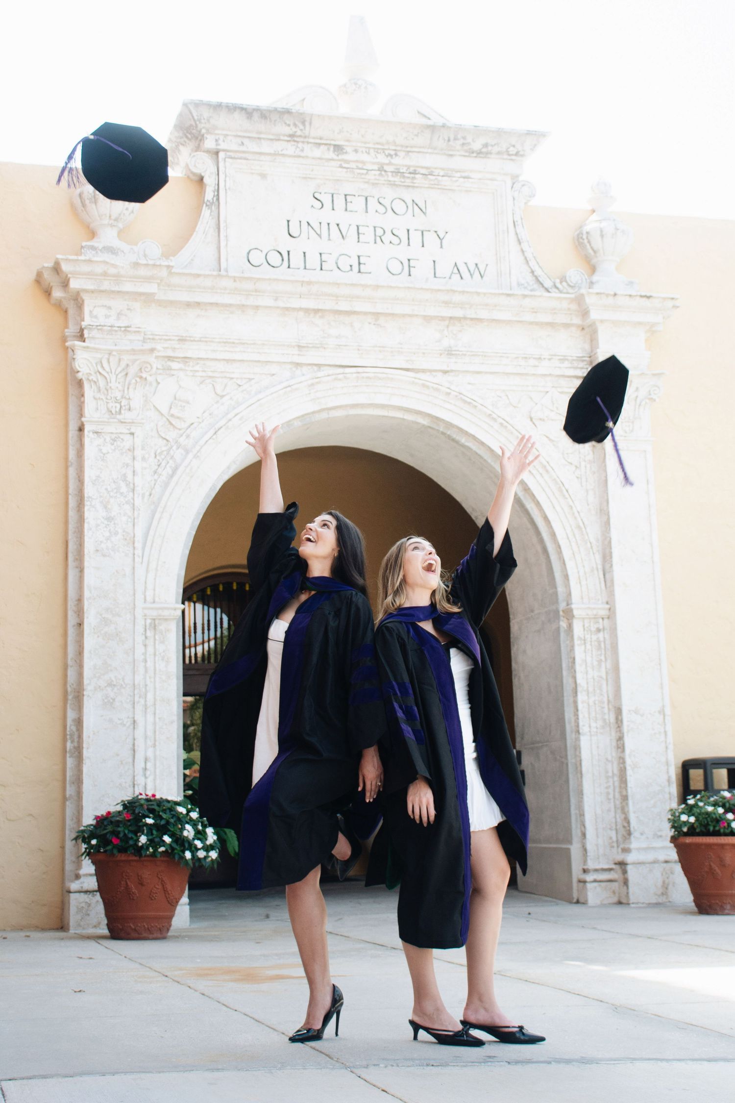 Graduates celebrate by tossing caps in front of ornate university archway.