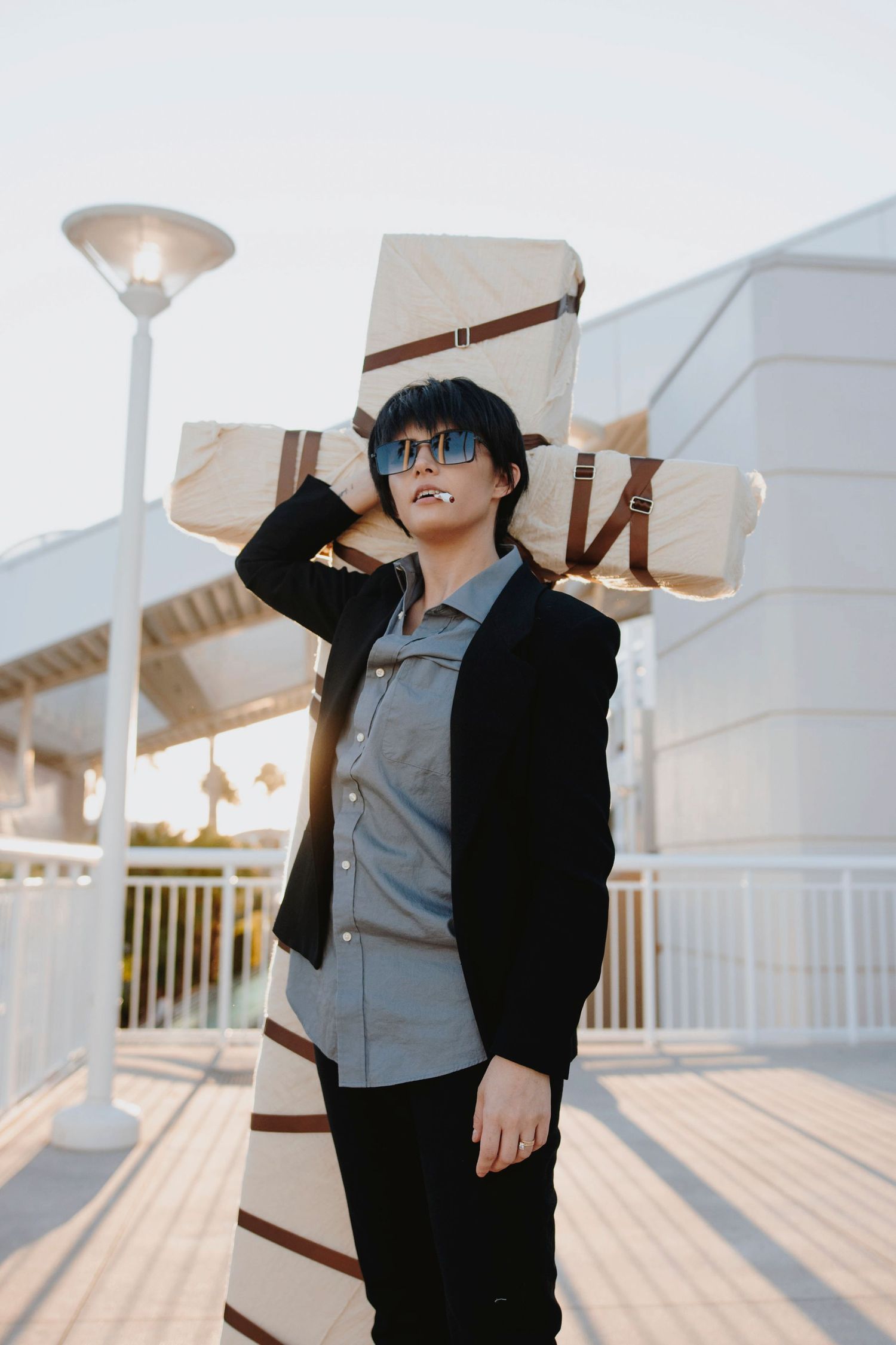 Cosplayer in black and gray outfit posing on a sunlit deck with dramatic shadows.
