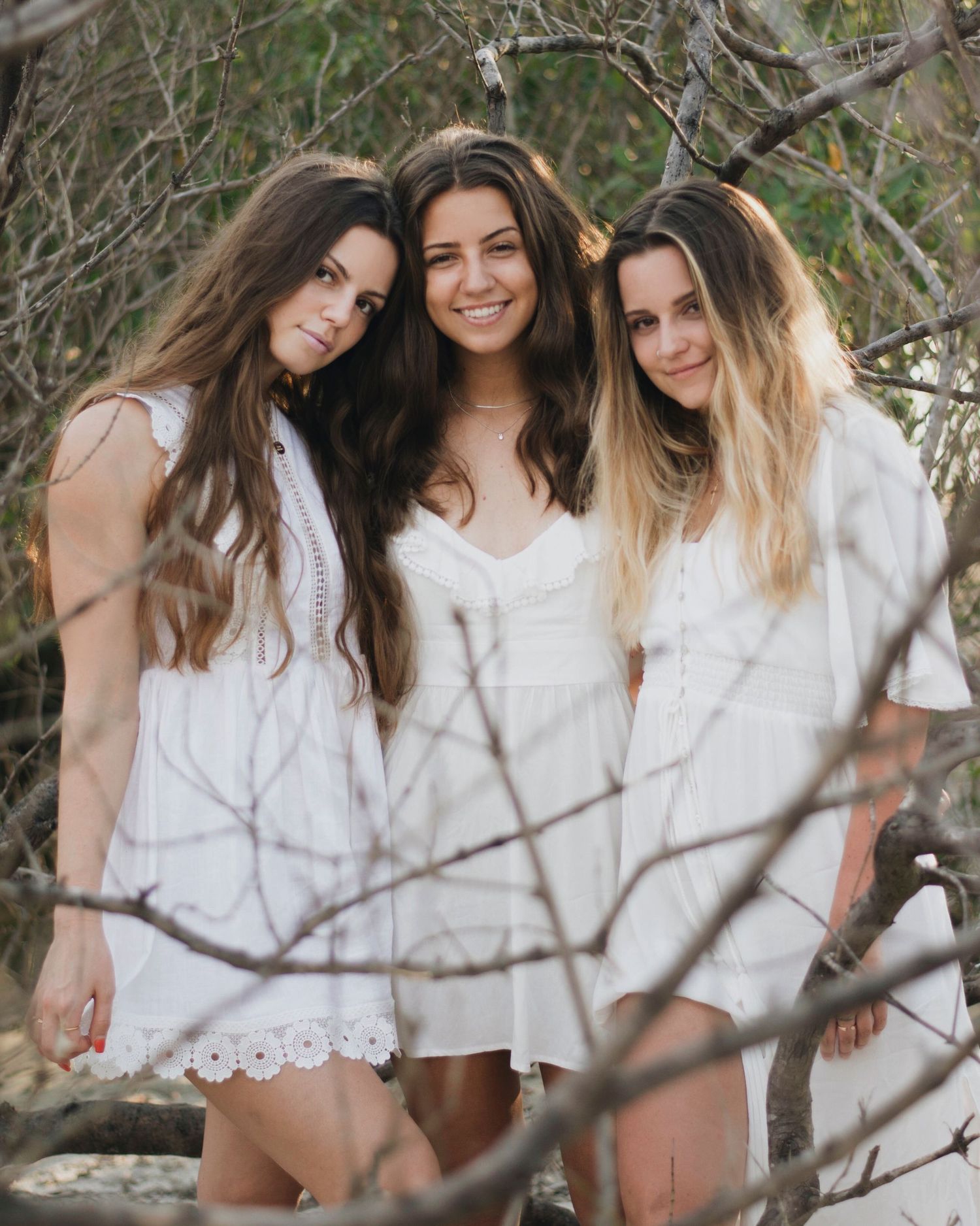 Three sisters in white outfits share joyful moments during outdoor photoshoot.