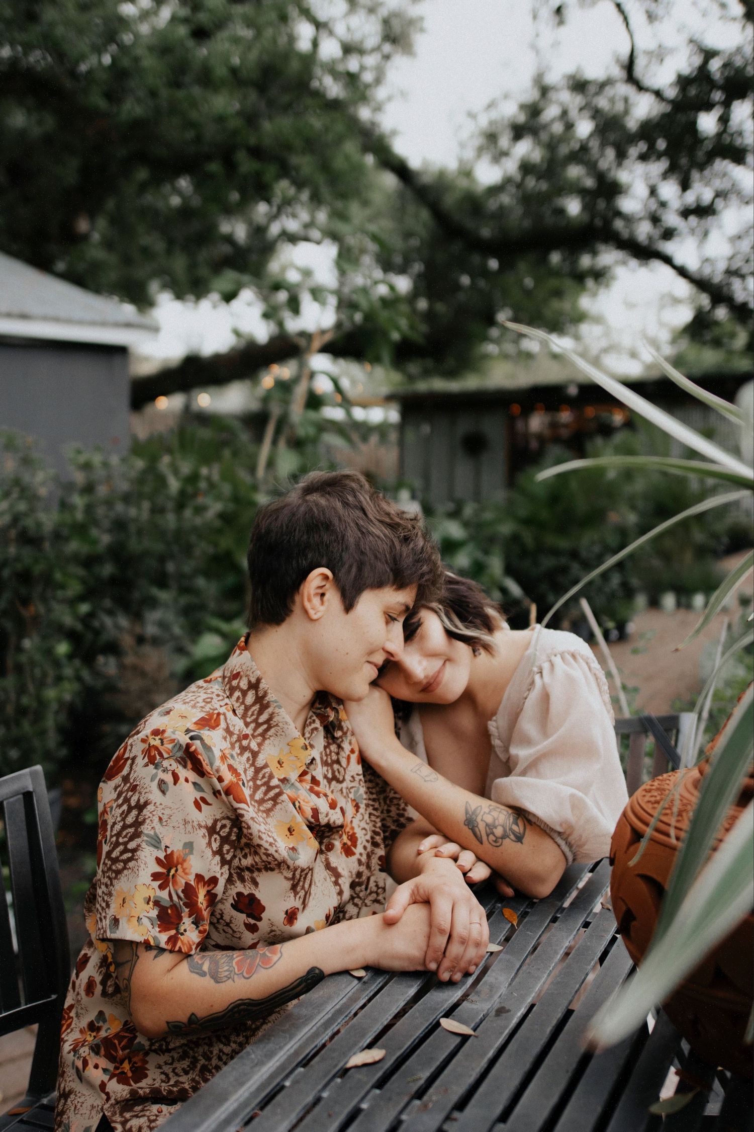 A couple sharing an intimate moment on a wooden bench surrounded by greenery.