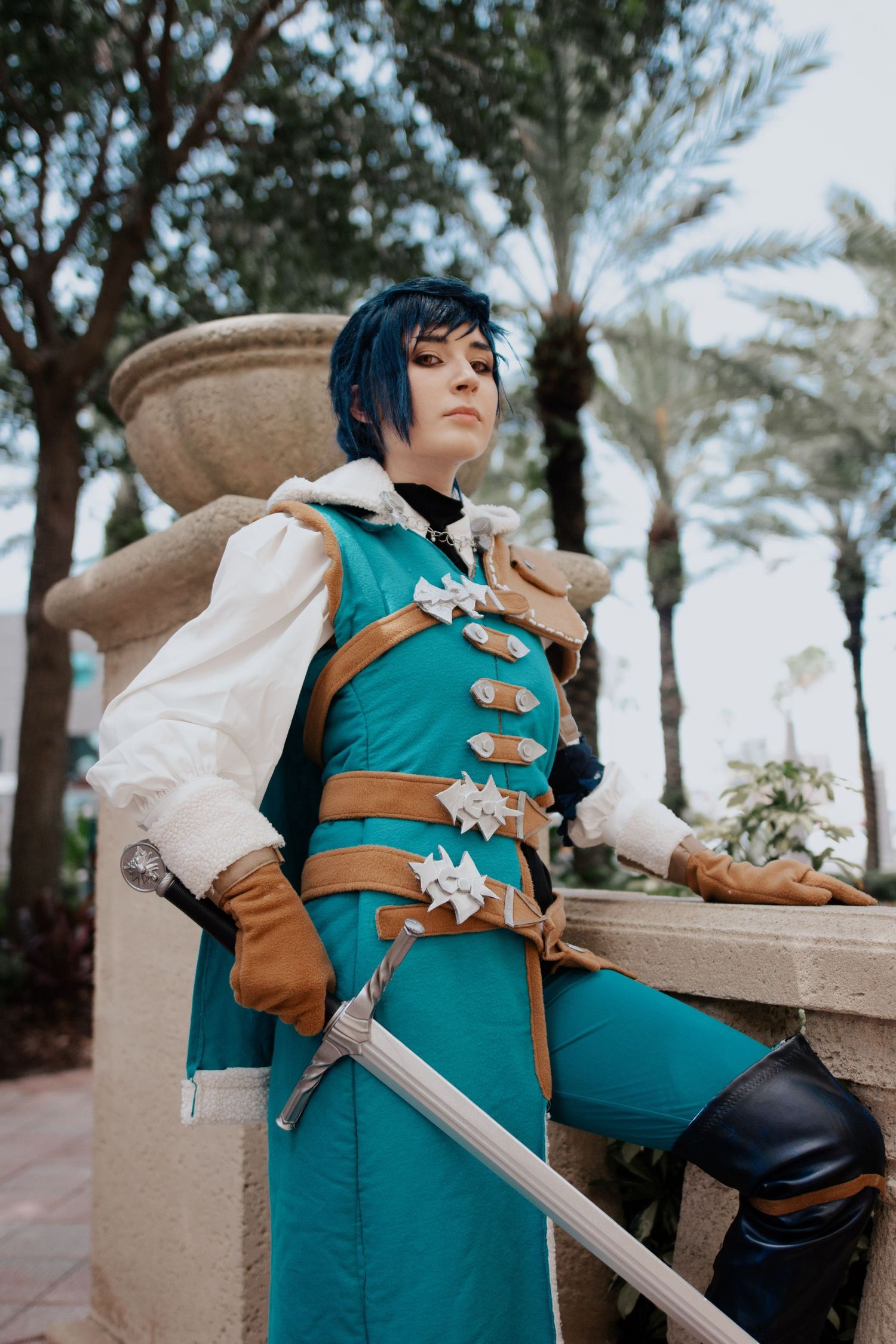 Medieval fantasy cosplayer in teal and brown armor poses with sword outdoors.